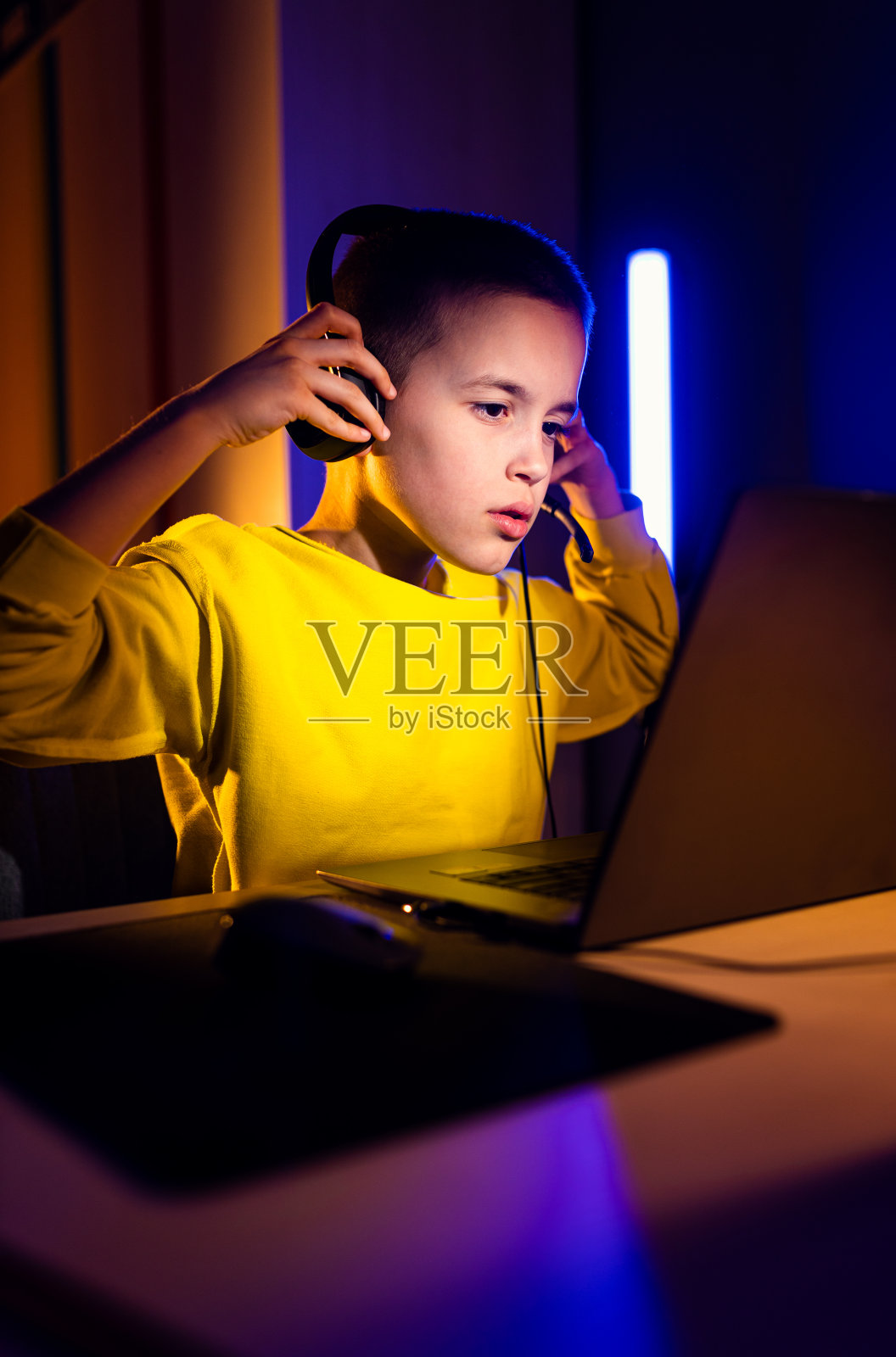 年轻兴奋的男孩玩家戴着耳机在家里的笔记本电脑上玩视频游戏。照片摄影图片