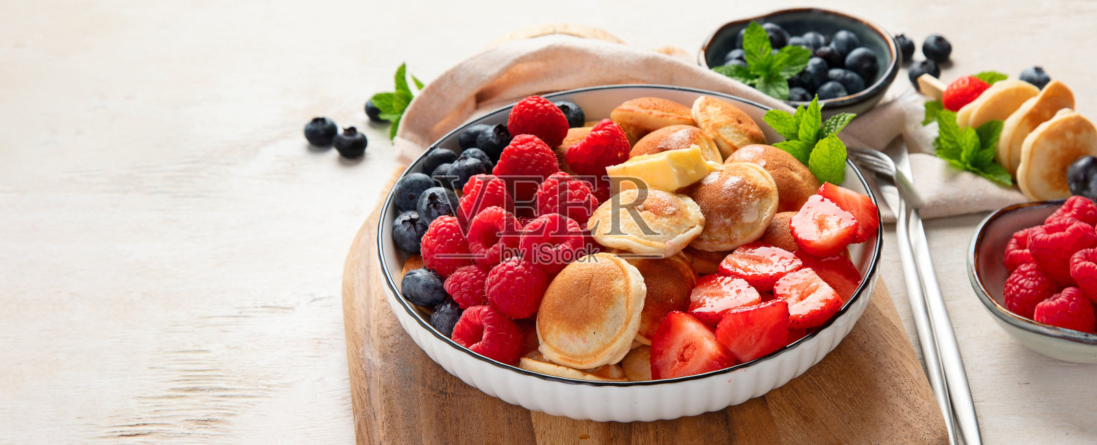 美味的蓝莓,草莓和覆盆子煎饼。甜美可口的早餐在浅色的背景照片摄影图片