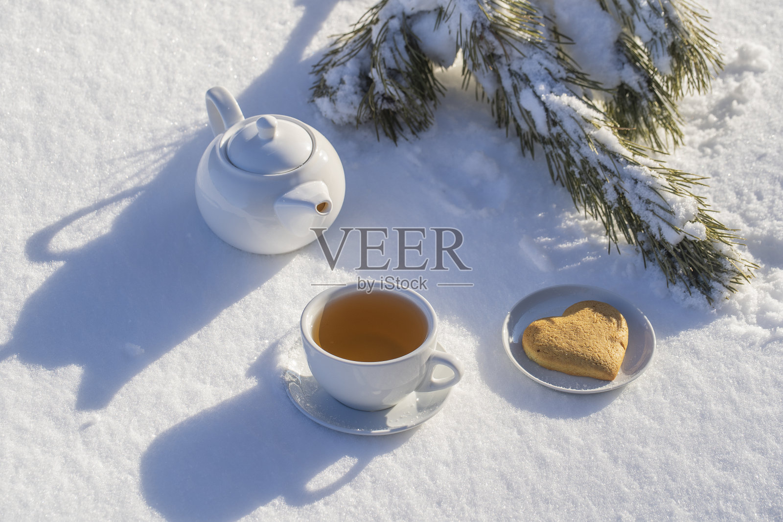 白色的热茶杯和茶壶在床上的雪和白色的背景,近距离照片摄影图片