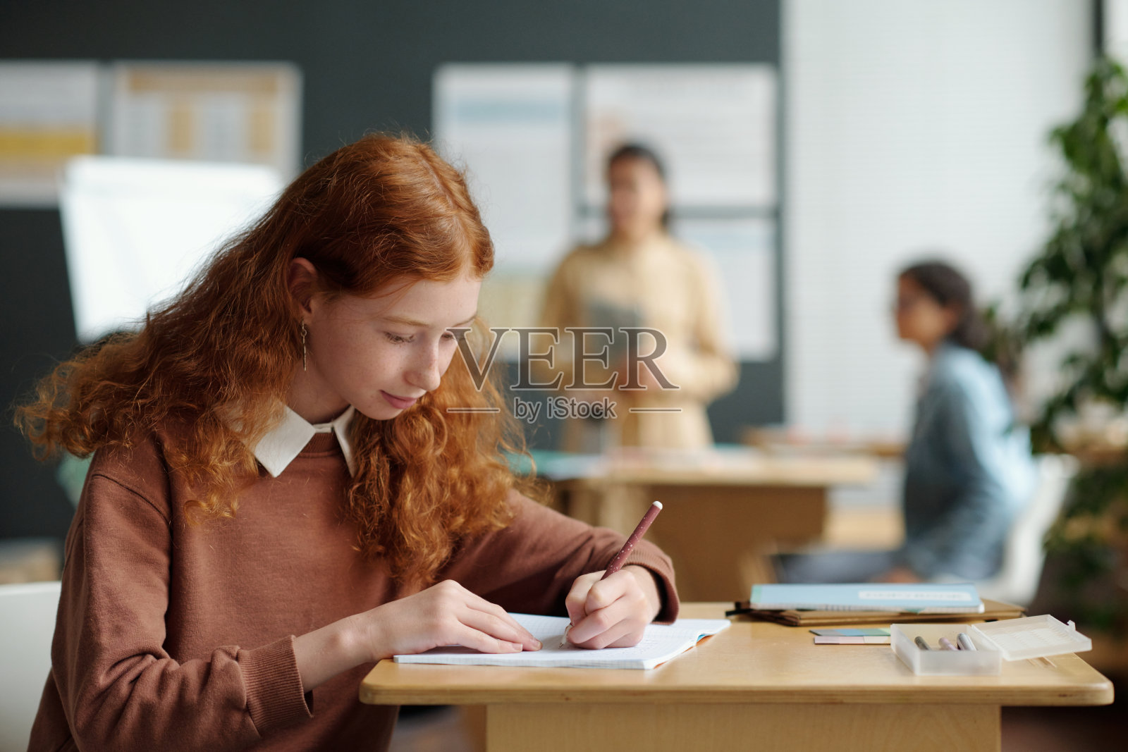 长着一头红卷发的可爱女学生在抄写本上做笔记照片摄影图片