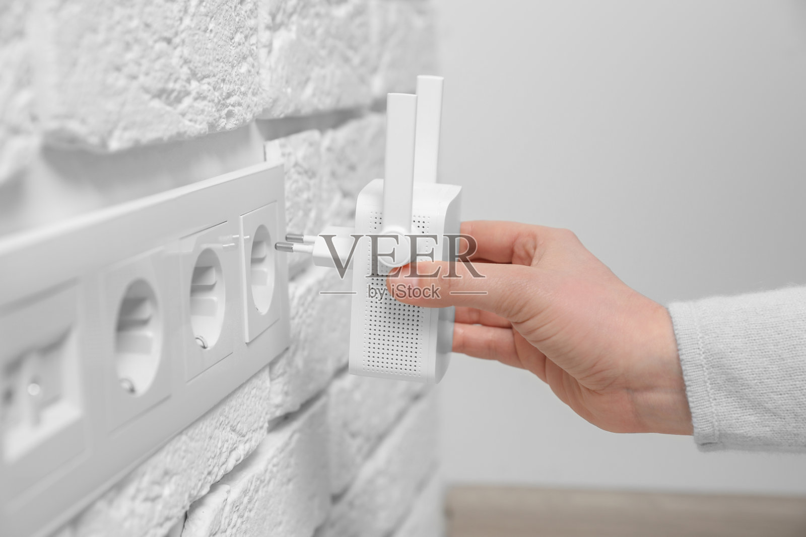 一名妇女将无线Wi-Fi中继器插入室内电源插座,特写照片摄影图片