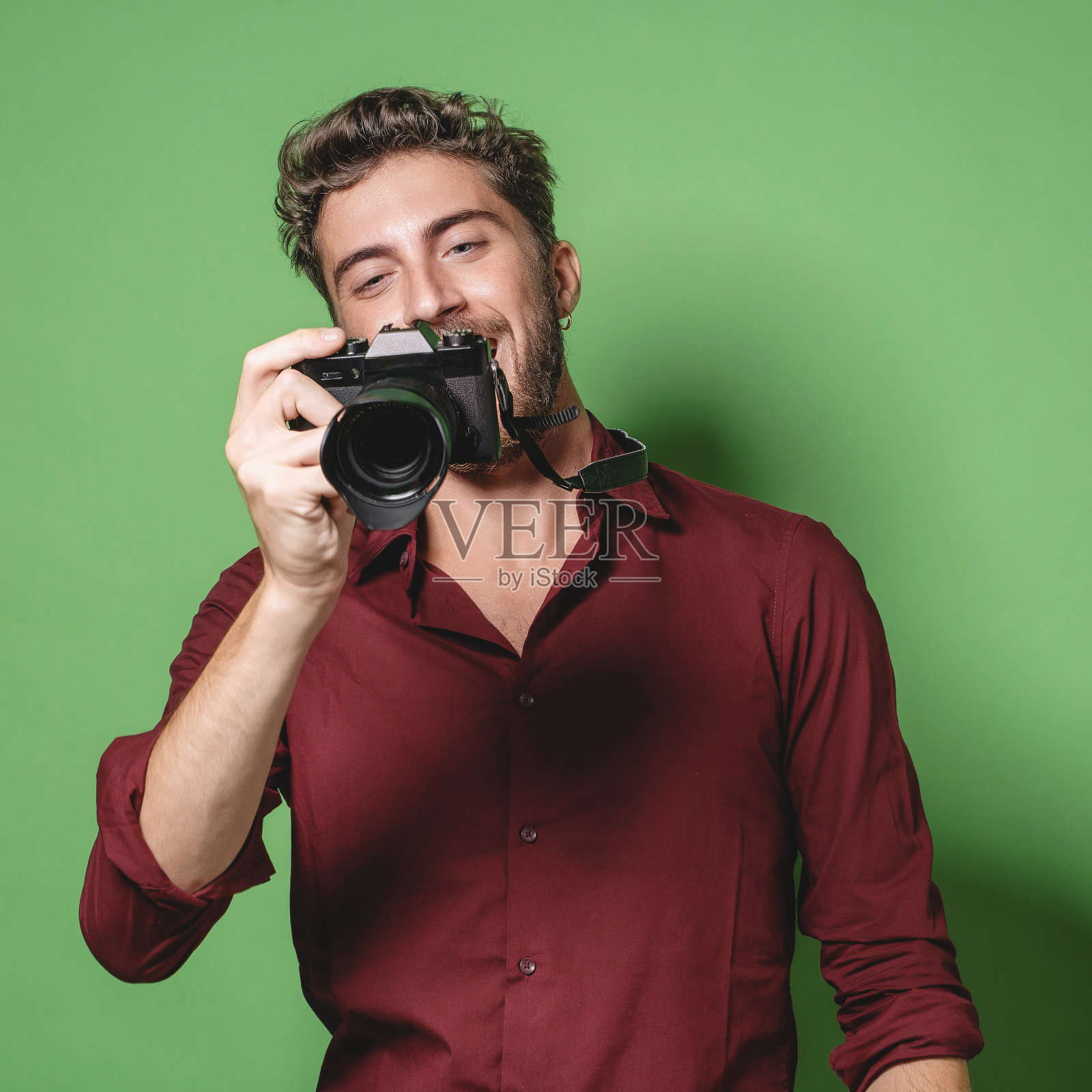 时髦的帅哥摄影师回顾照片从无反光镜相机-孤立的绿色背景照片摄影图片