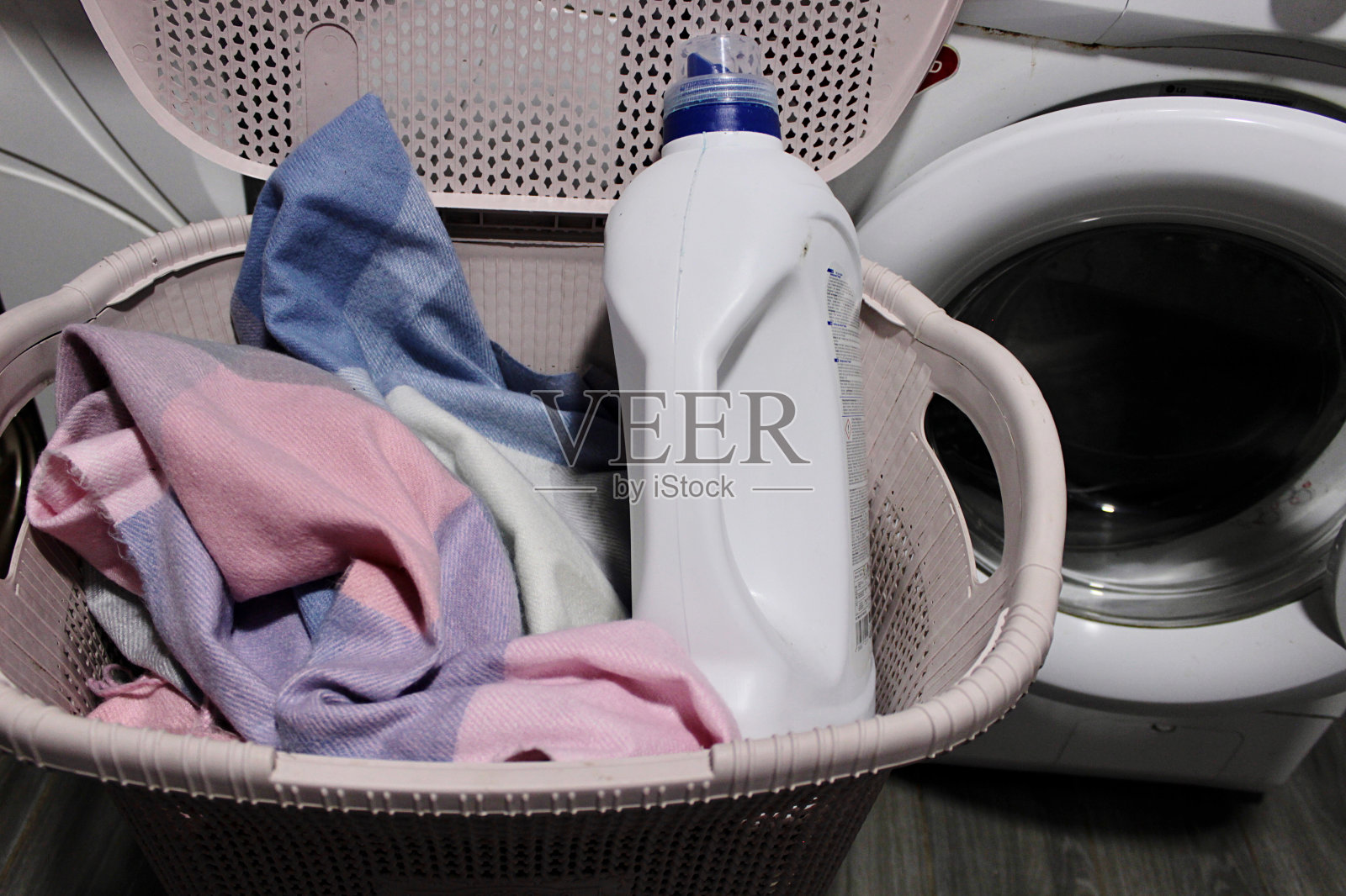 在浴室里,洗衣机旁边有一个粉红色的篮子,里面装着脏衣服和洗衣粉照片摄影图片