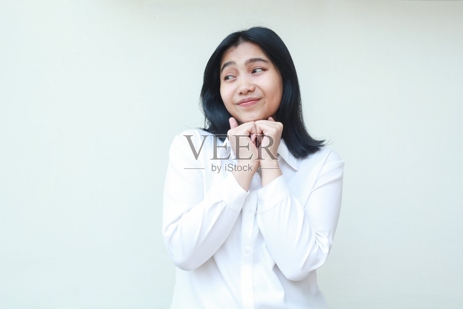 正念感恩的亚洲女CEO的形象,穿着白色正装衬衫,激动地把拳头放在下巴上,看着别处,思考着想法和战略,站在孤立的背景上感到很舒服照片摄影图片