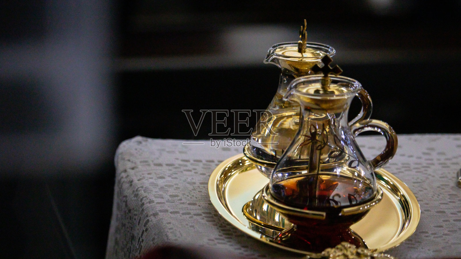 一对透明的玻璃小瓶,盛有水和酒,放在金色的立盘上,黑色的木桌上铺着白色的桌布照片摄影图片