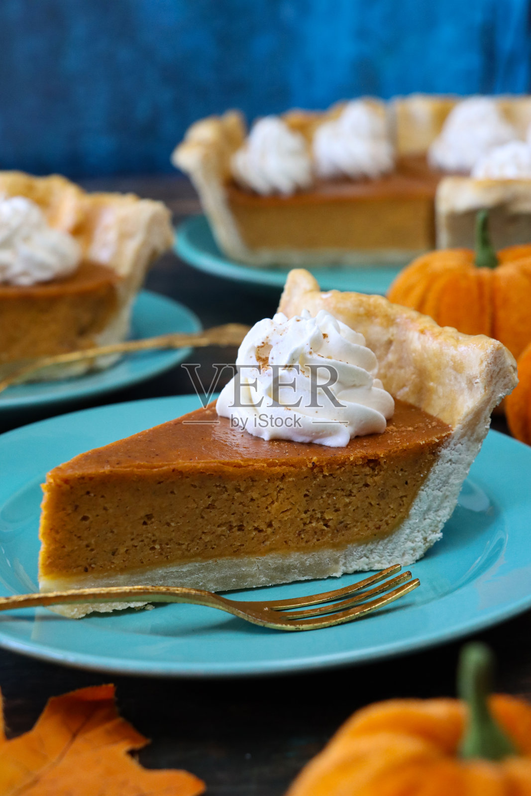图像切片新鲜出炉的南瓜派顶部与漩涡生奶油在蓝色盘子,挞锡盒包含切割自由形状的凹槽派皮填充南瓜泥,毛绒南瓜,木纹表面,绿色背景,重点在前景照片摄影图片