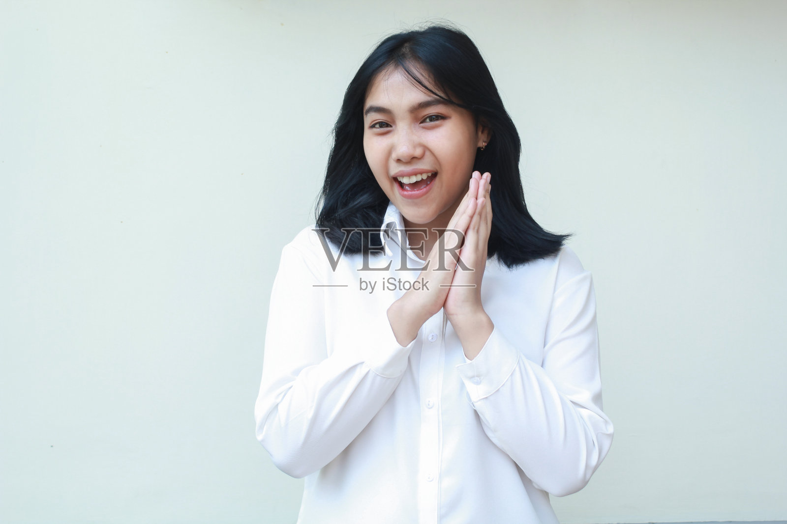 顽皮成功的亚洲年轻女商人双手合拢,穿着白色西装正装衬衫,自信地看着镜头,脸上带着兴奋的表情,站在孤立的背景上照片摄影图片