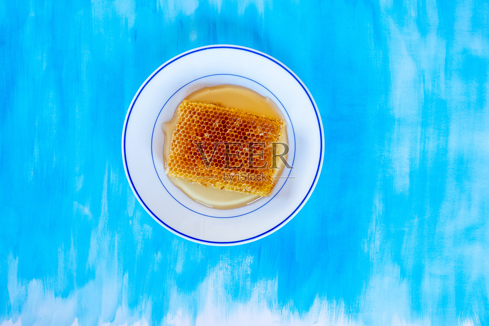 蓝色背景下的蜂蜜碗照片摄影图片