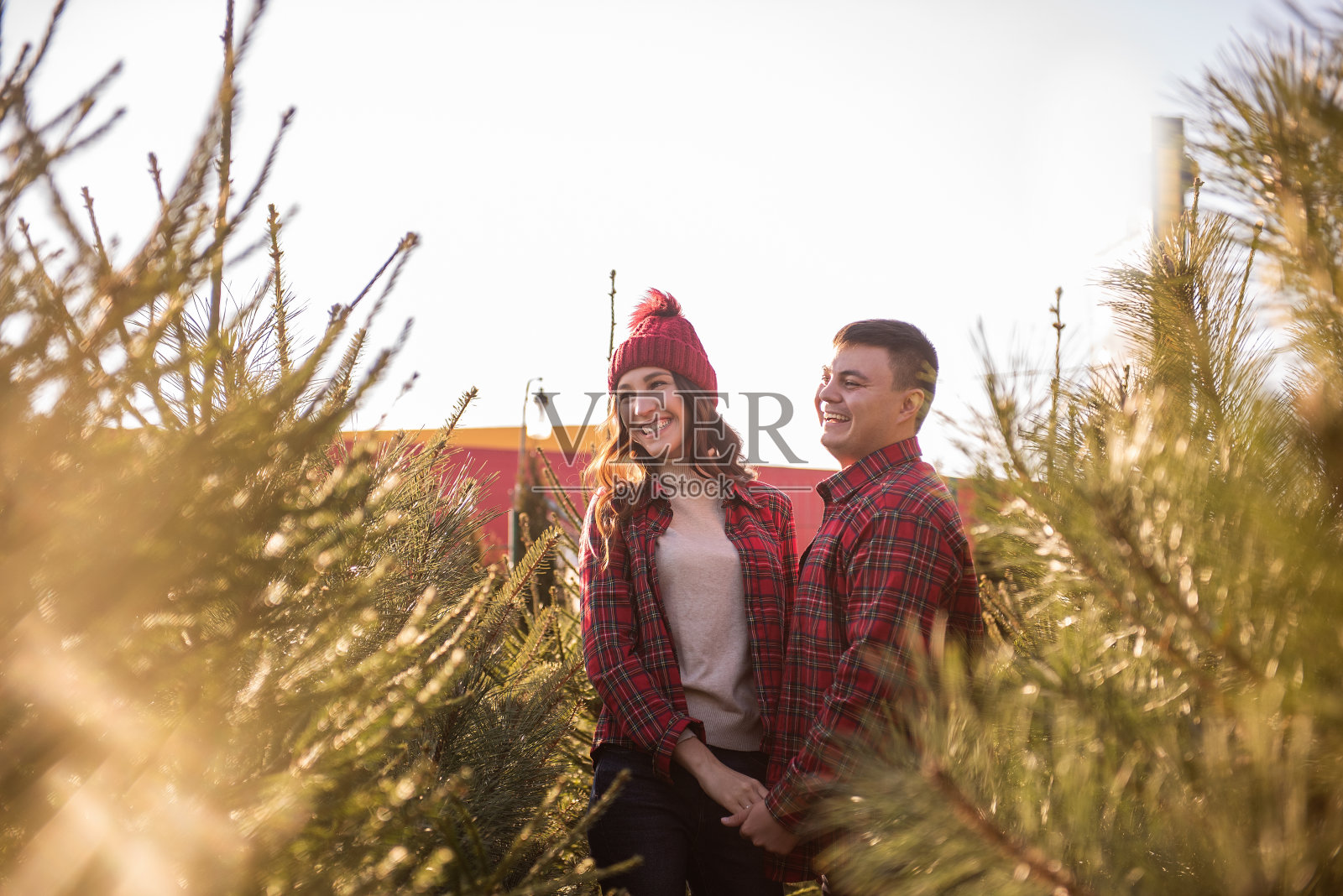 穿着红色格子衬衫、编织着帽子的情侣们在圣诞树市场上嬉闹着照片摄影图片