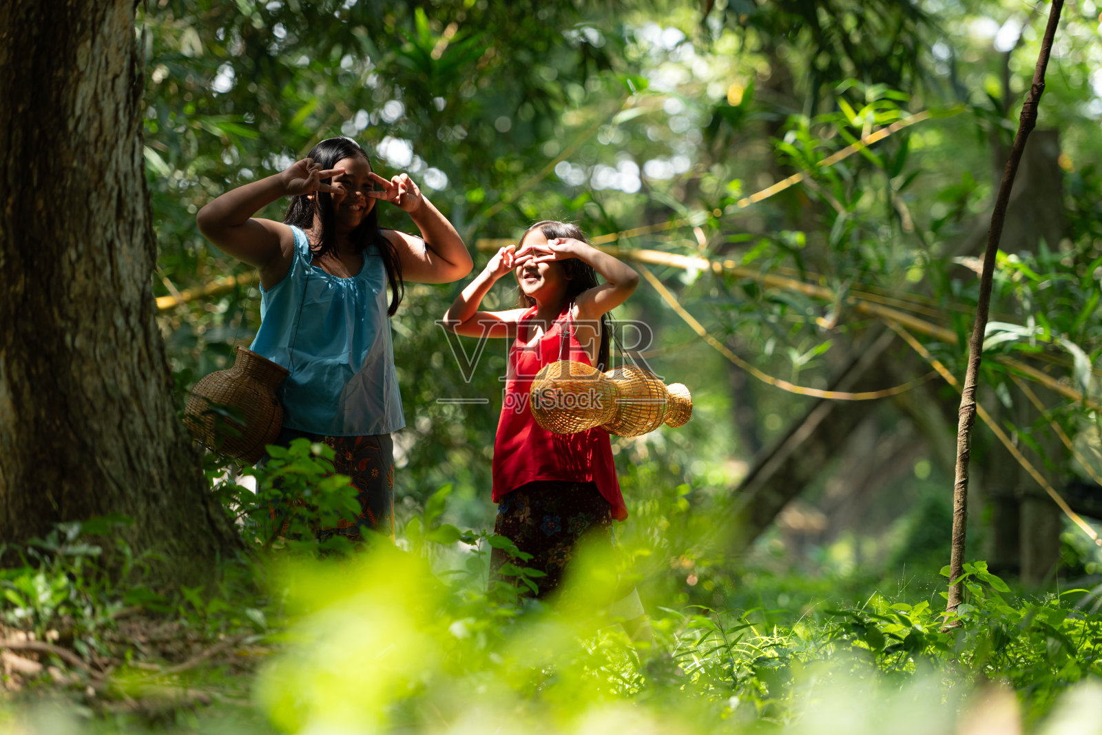 两个穿着传统服装的亚洲女孩站在雨林中。他们在一起玩得很开心,然后帮爷爷在附近的湖里钓鱼。照片摄影图片