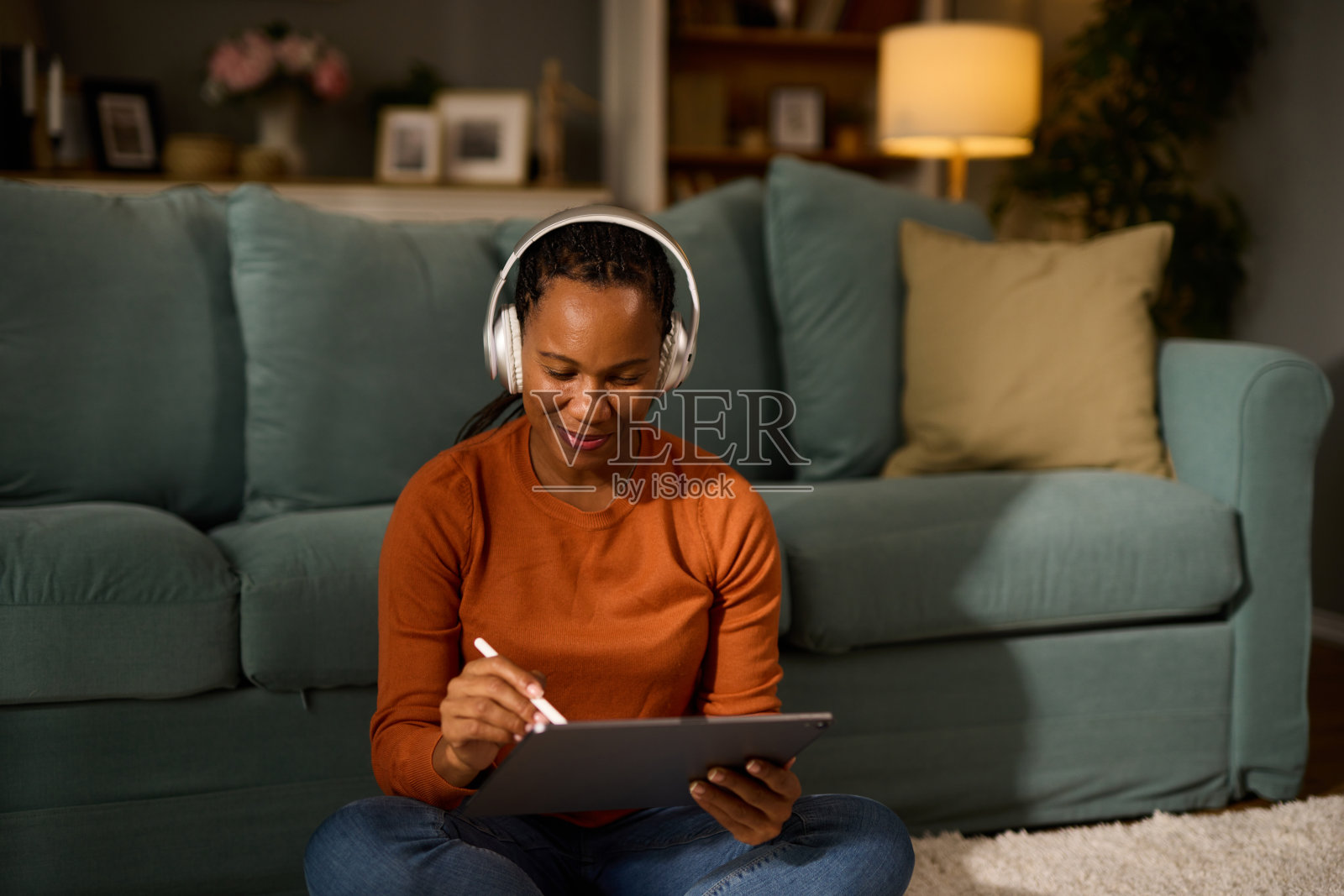 在家放松时戴着耳机使用平板电脑和数字笔的女人照片摄影图片
