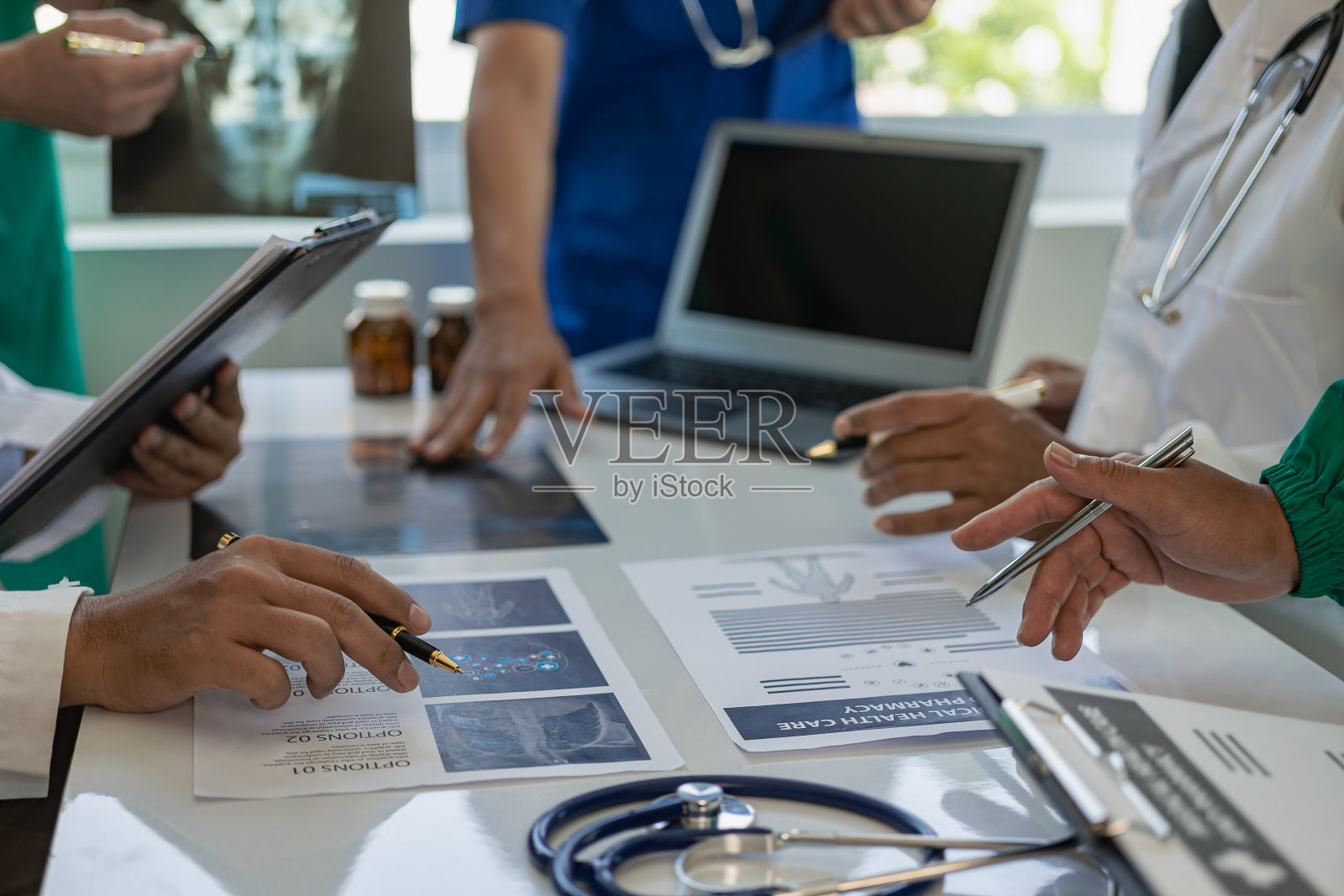 与穿着白大褂和外科手术服的医生会面,坐在桌子旁讨论病人的记录。医生团队致力于数字平板电脑,医生平板电脑技术使用电脑照片摄影图片