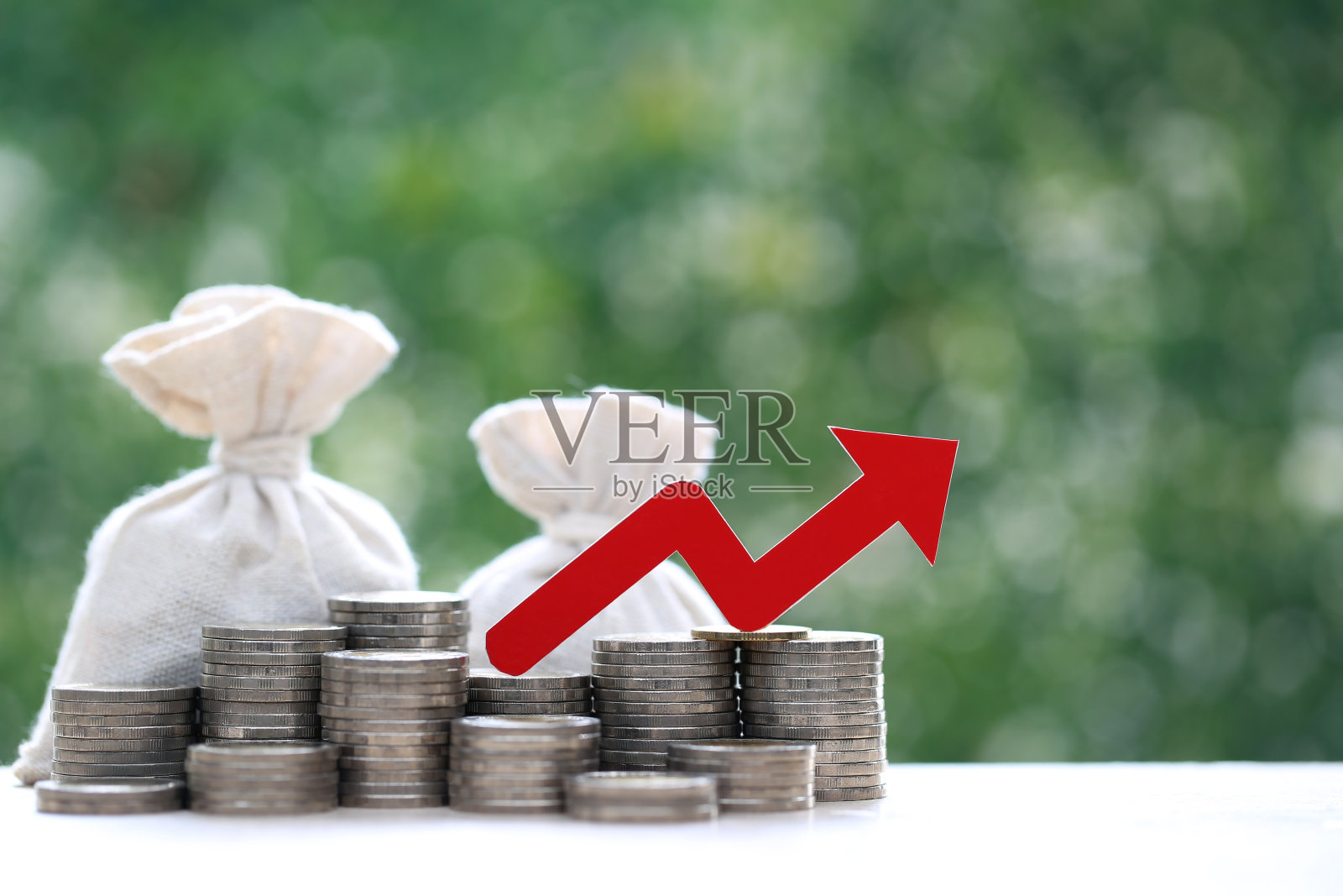 红色箭头图上的硬币,钱和钱袋堆叠在自然绿色背景,商业投资和风险管理的概念。财务风险评估照片摄影图片