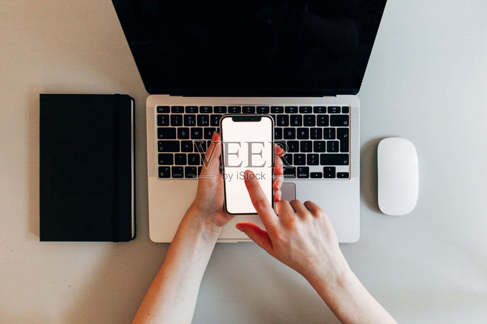 2020年中期,女性手持智能手机,在现代办公桌上的2020年笔记本电脑前-手机模拟-自上而下-使用食指照片摄影图片