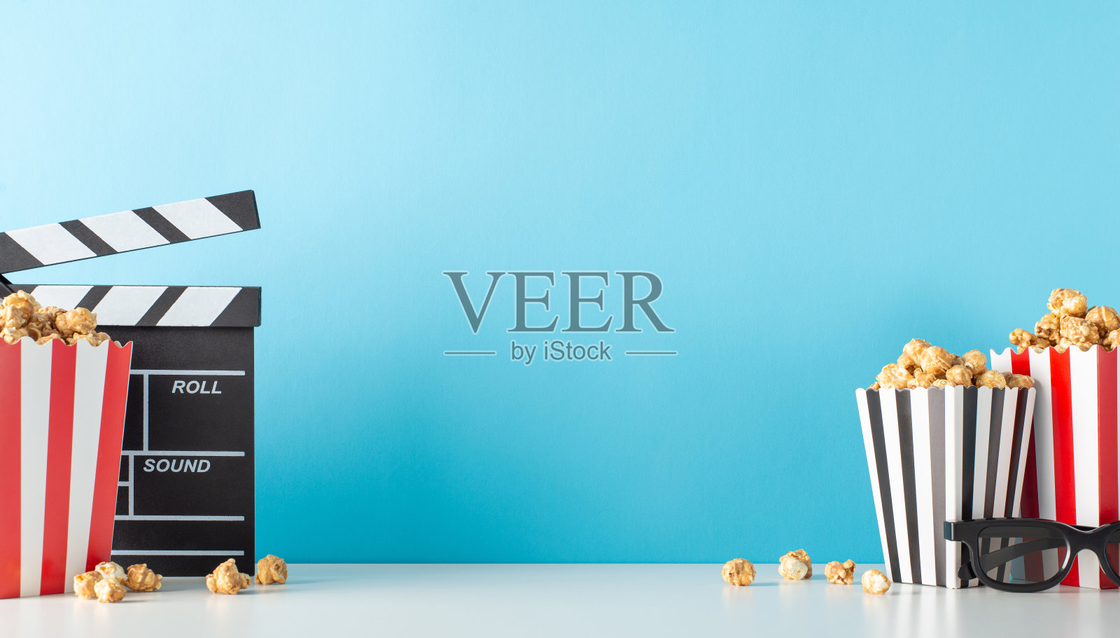 提升你的电影首映使用愉快的零食主题。捕捉桌子的侧视图,电影导演的拍手,3D规格,美味的爆米花在柔和的蓝色背景下,留出空间给电影广告照片摄影图片