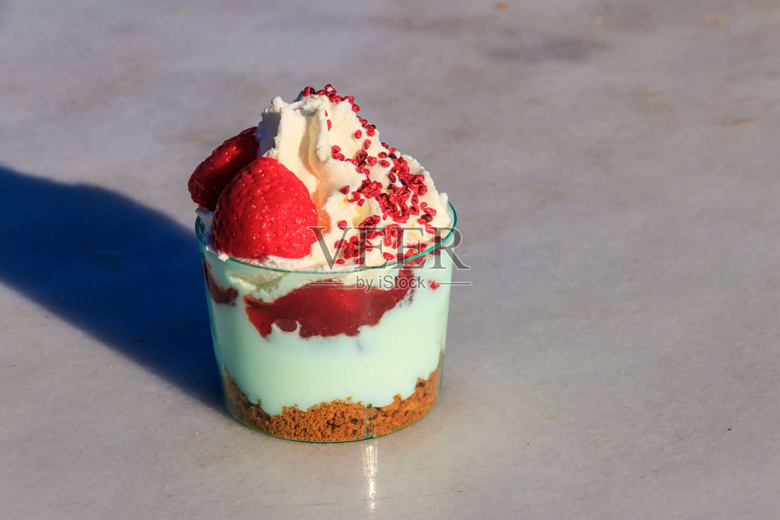 草莓松糕,加鲜奶油、浆果酱和饼干屑,装在玻璃杯里,背景是灰色的混凝土照片摄影图片