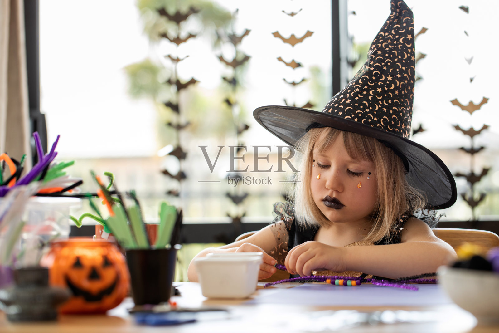孩子们的万圣节派对。一个穿着女巫服装的女孩在万圣节制作装饰房子的手工艺品照片摄影图片