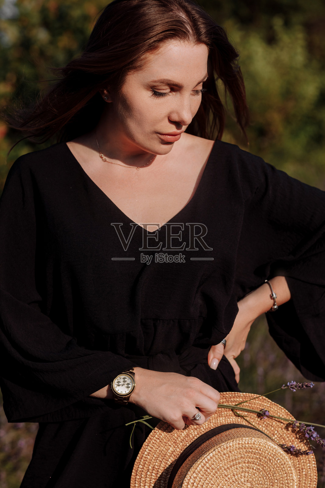 穿着黑色连衣裙的年轻性感女子的肖像坐在盛开的紫色薰衣草田,看着镜头。迷人的黑发女孩享受生活和梦想。自然美理念照片摄影图片