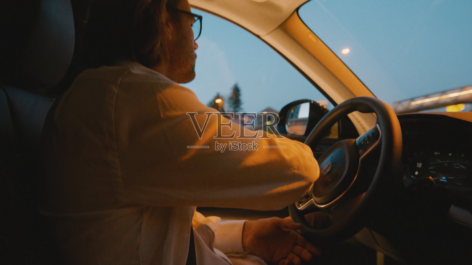 黄昏时分,手持方向盘的年轻人在城市里开车的侧视图照片摄影图片