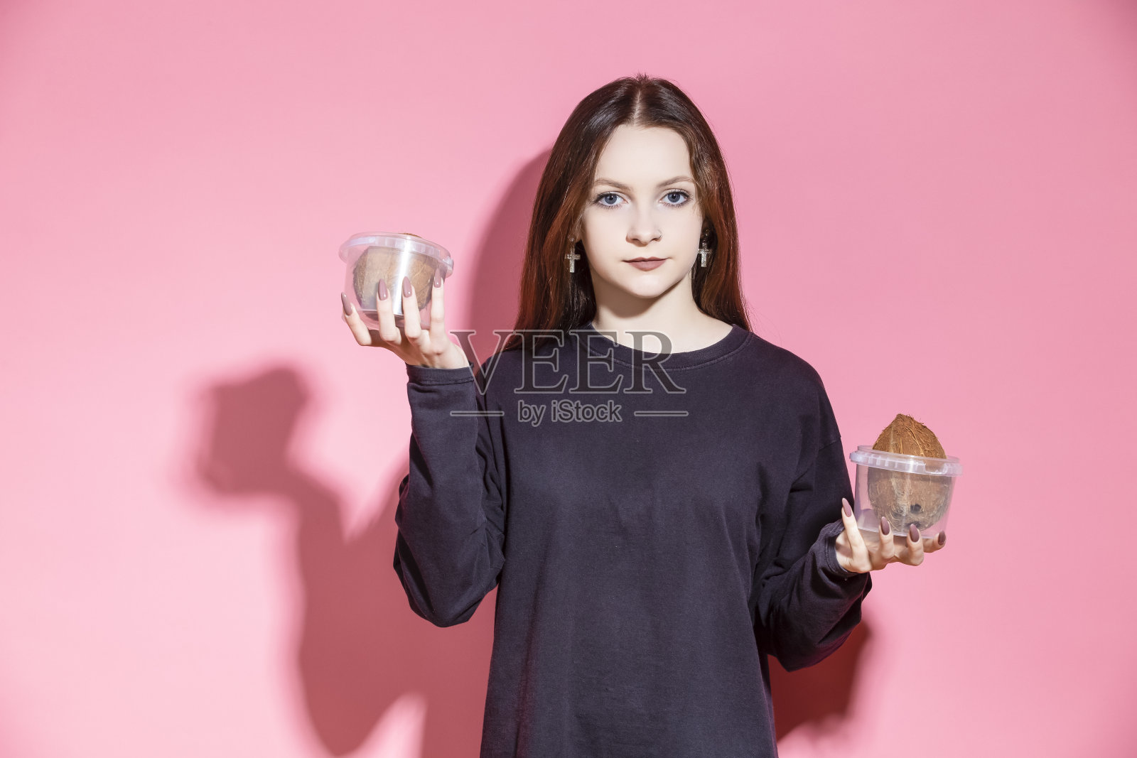 穿着黑色衬衫的迷人少女微笑着在室内用手拿着放在塑料容器里的椰子摆姿势。照片摄影图片