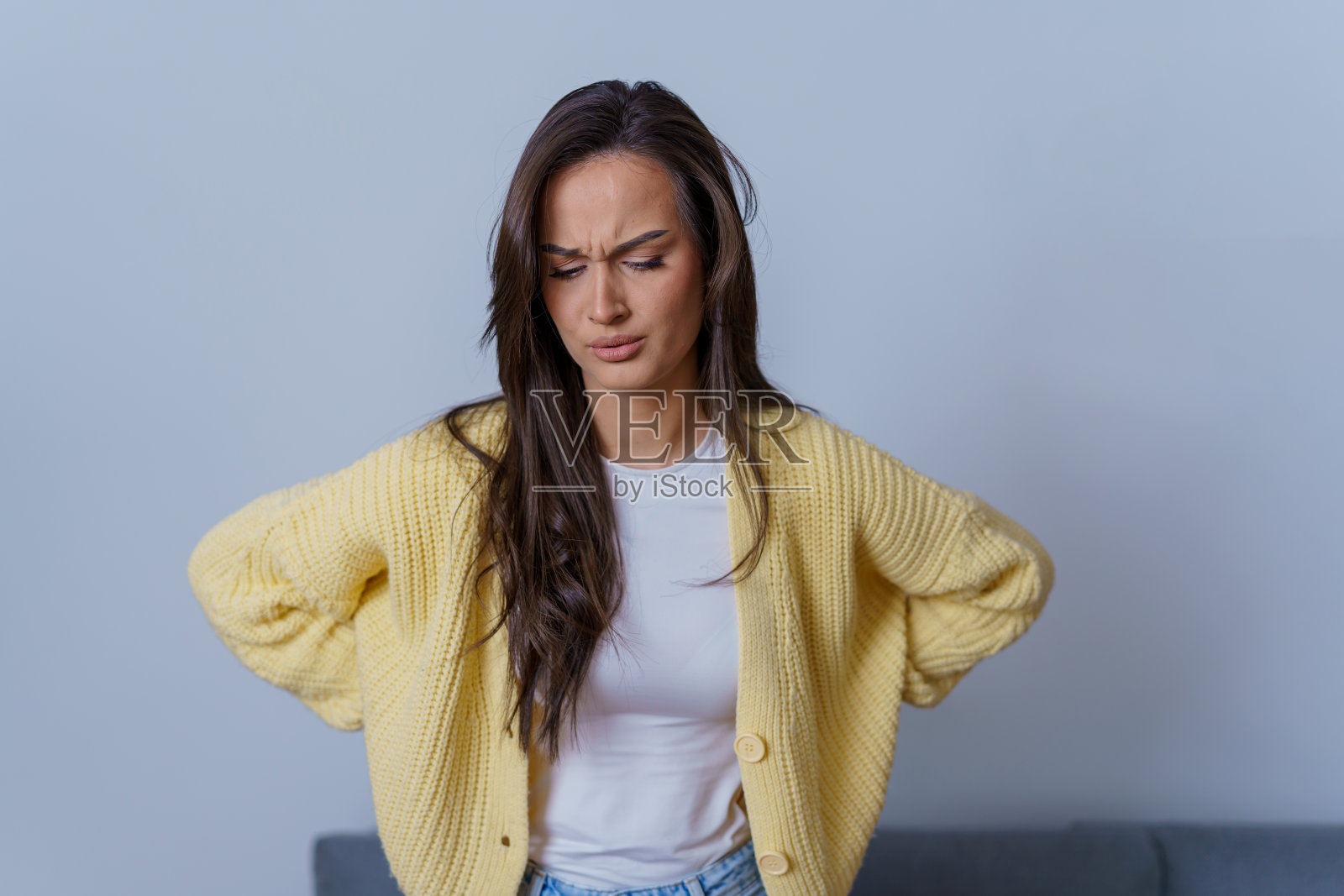 一名年轻女子正因背痛而坐在沙发上,用手托着她的下背部照片摄影图片