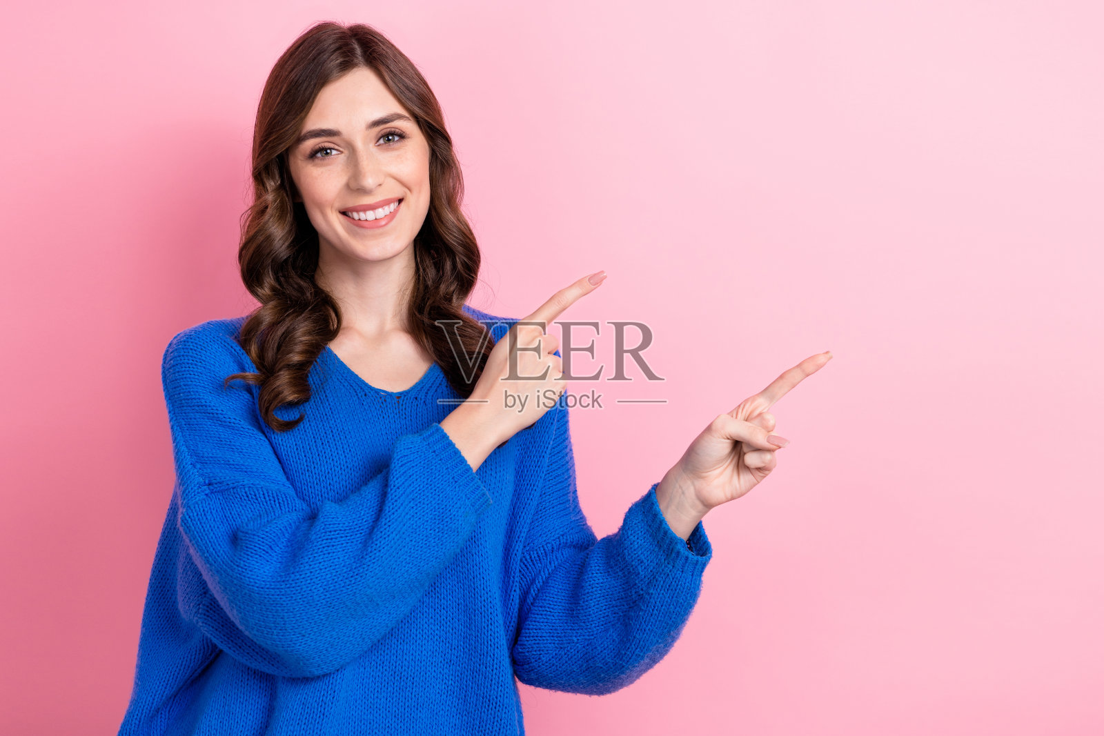 可爱的满意的女孩穿着时髦的衣服,两只手臂展示海报的好消息,空白的空间孤立在粉红色的背景照片摄影图片