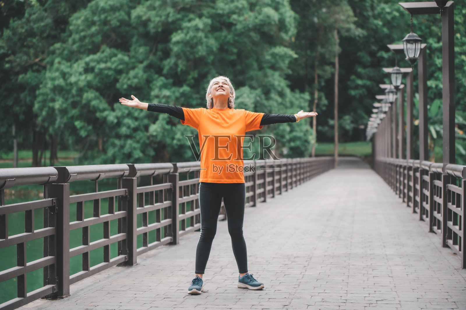 一位白发苍苍的亚洲老妇人清晨在公园里锻炼时伸开双手呼吸新鲜空气。照片摄影图片