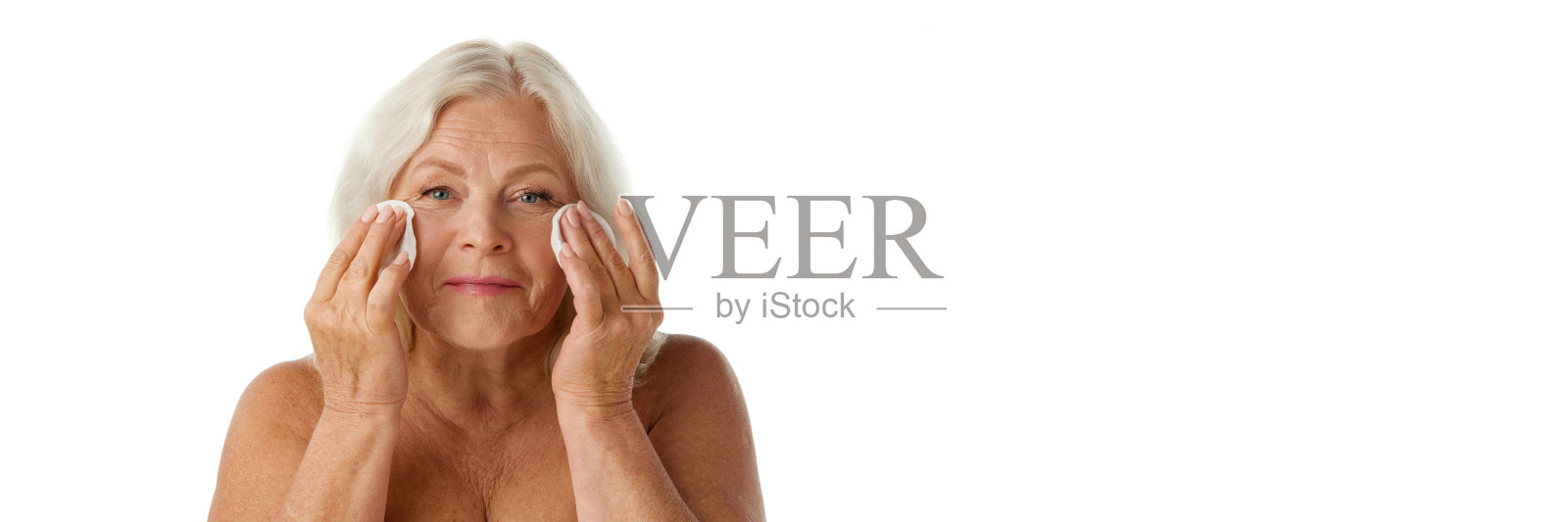 有皱纹的漂亮老年妇女,在白色的工作室背景下用化妆棉卸妆照片摄影图片