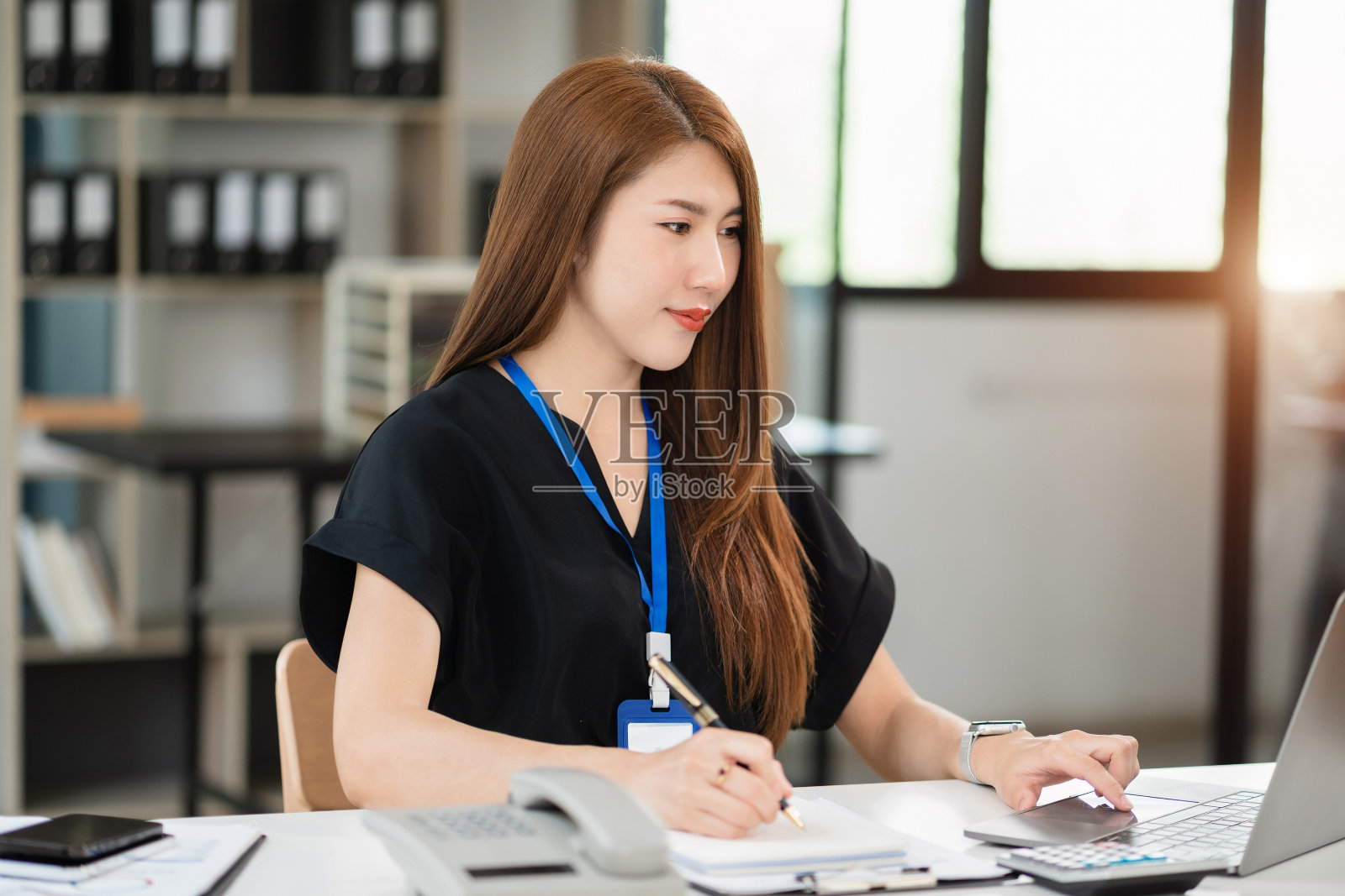 女性在早上使用智能手机和笔记本电脑在办公桌前工作。照片摄影图片