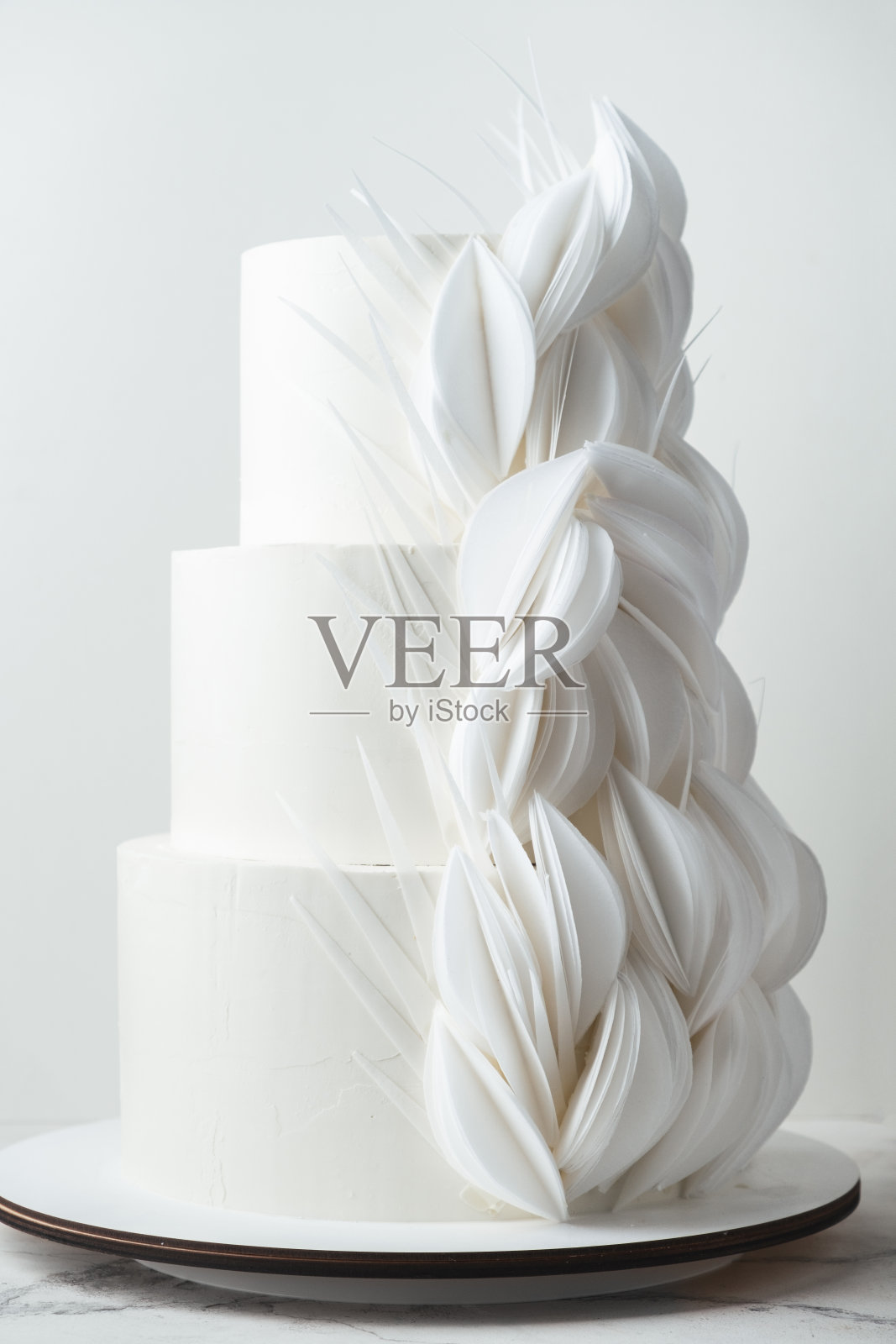 三层婚礼蛋糕,白色巧克力糖衣,用可食用的威化纸做成的花装饰。白色背景照片摄影图片