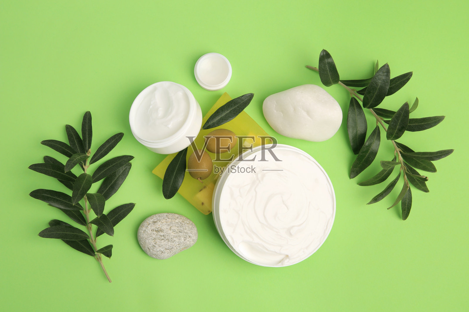 不同的化妆品与橄榄和石头在浅绿色的背景,平躺照片摄影图片