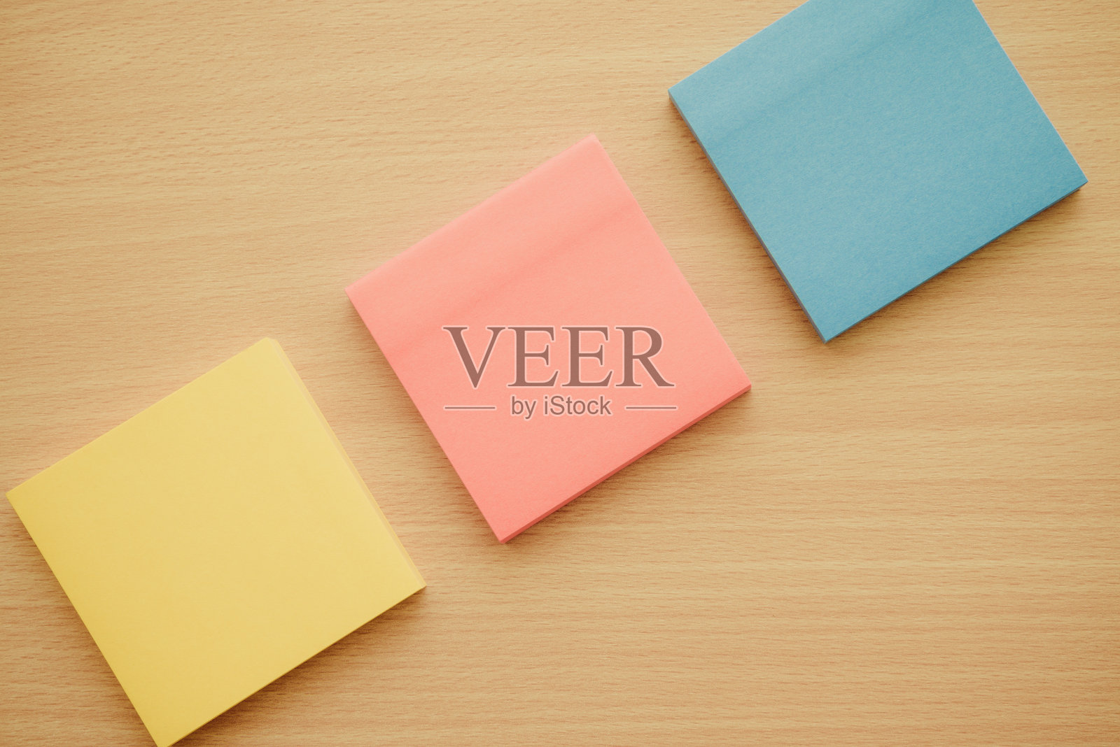 在木制背景上平铺彩色方块胶纸。照片摄影图片