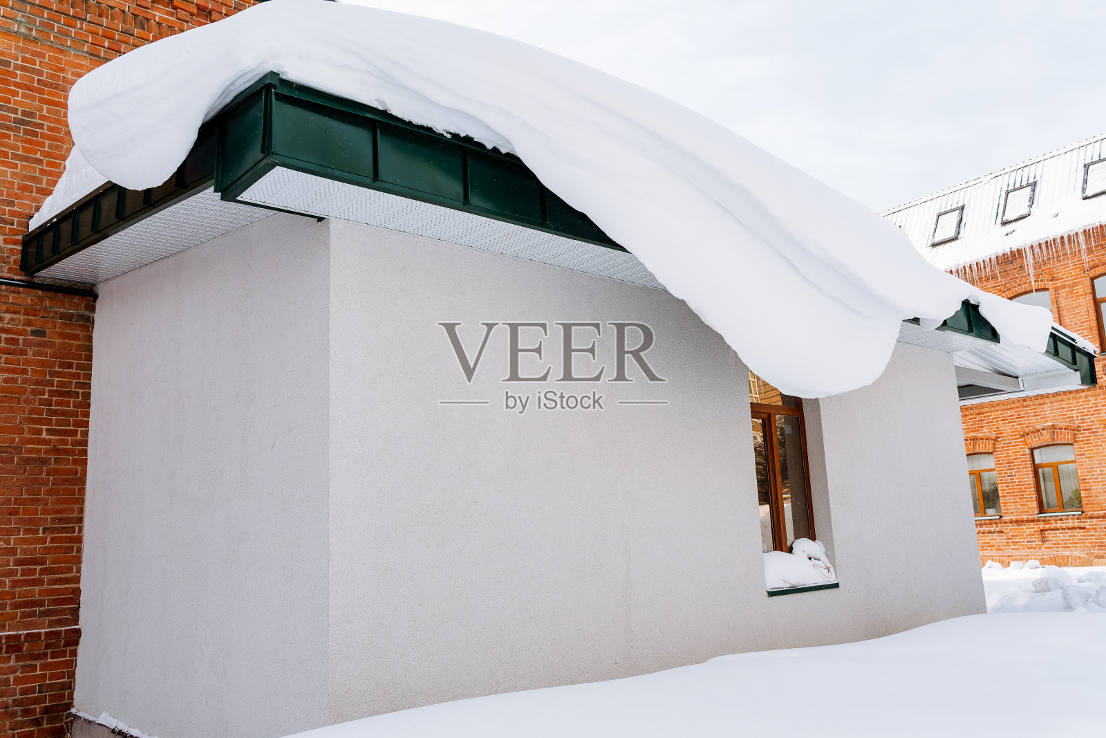 雪堆从屋顶垂下来。建筑物正面的雪块。冬天打扫街道。积雪下的城市建筑。冬天的到来照片摄影图片