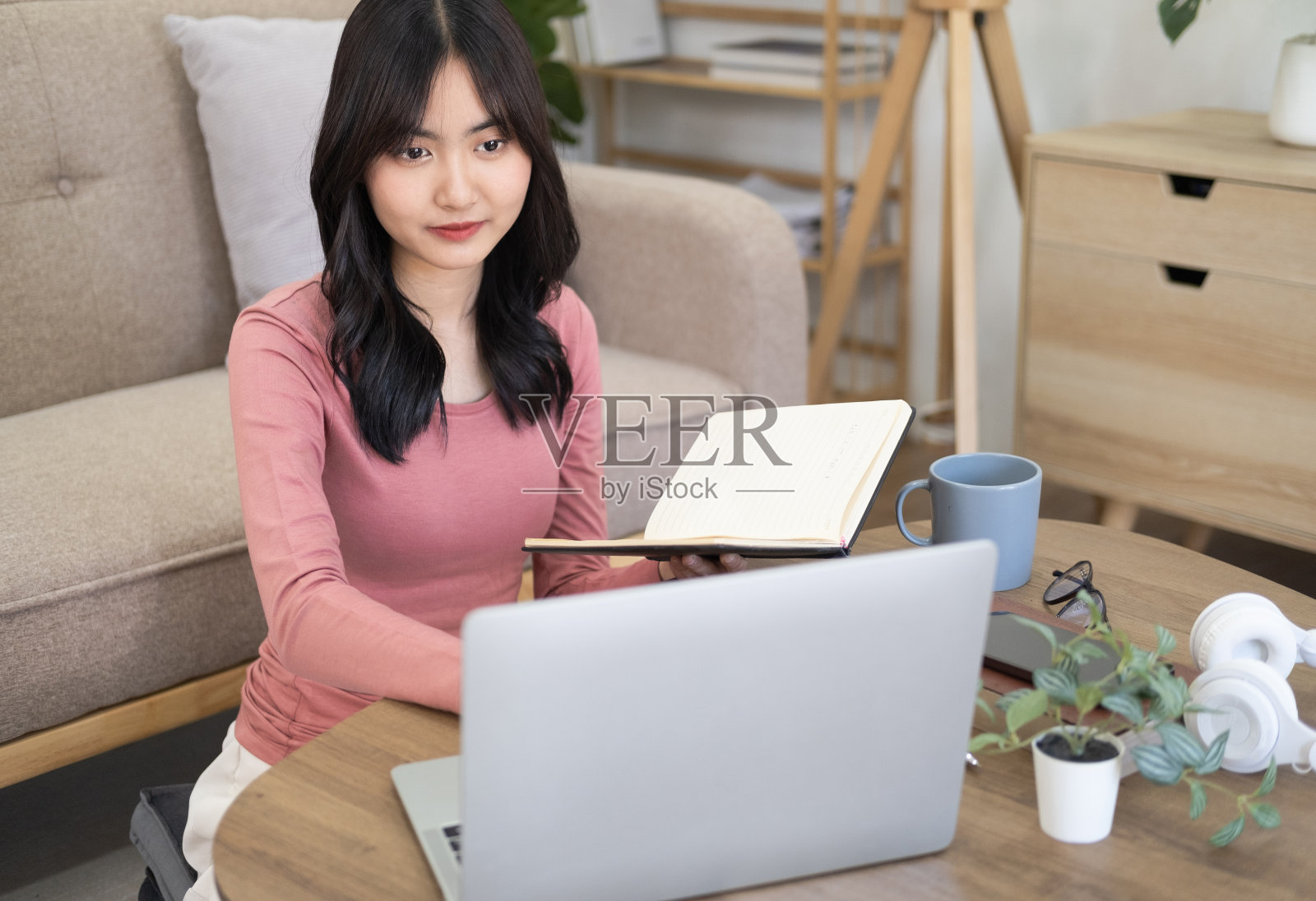 专注的年轻亚洲女商人或学生看着笔记本电脑拿着书本学习,严肃的女性工作或学习与电脑做研究或准备考试在线。照片摄影图片