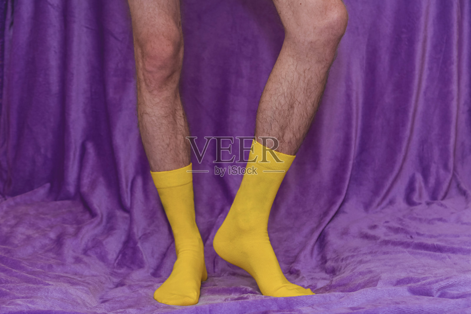 紫色背景上一个穿黄袜子的男人的腿。照片摄影图片