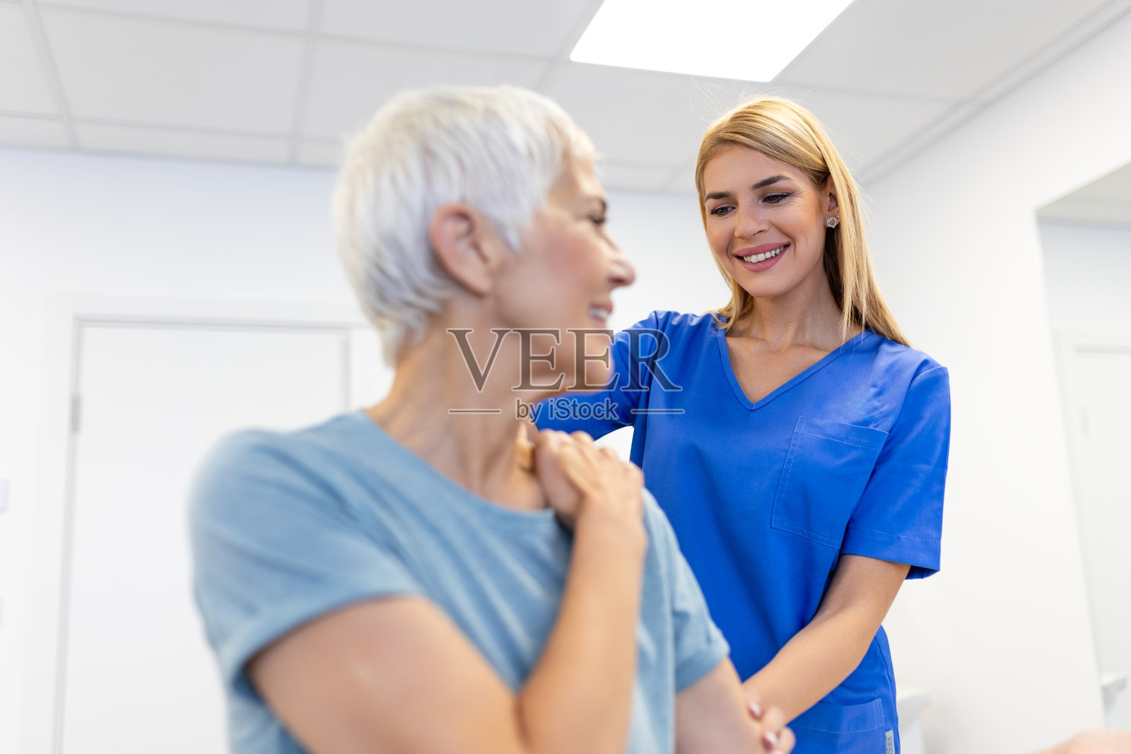 快乐的老年妇女和理疗师一起做运动。一位退休的老妇人在私人教练的帮助下在诊所做伸展手臂。照片摄影图片