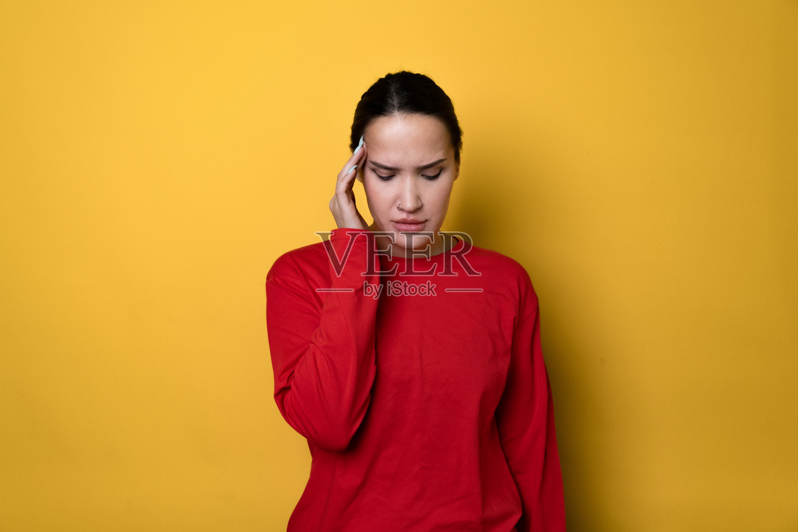 生病了,伤心了,疲倦了年轻漂亮的女人穿着红色的长袖,把手放在头上,揉太阳穴,头痛,患有偏头痛,孤立在普通的黄色背景工作室的肖像照片摄影图片