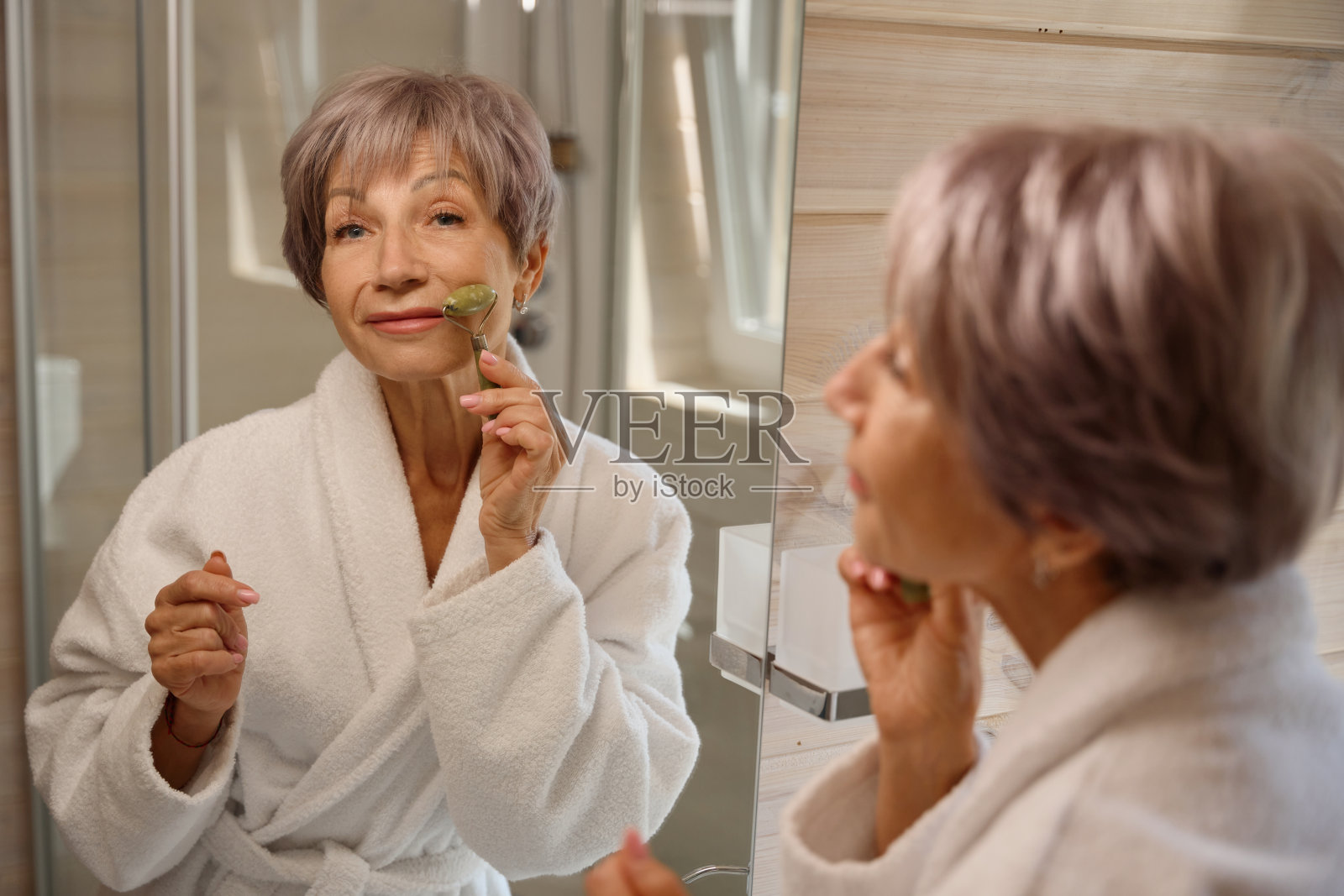 穿着浴袍的老妇人使用玉石面部按摩器照片摄影图片