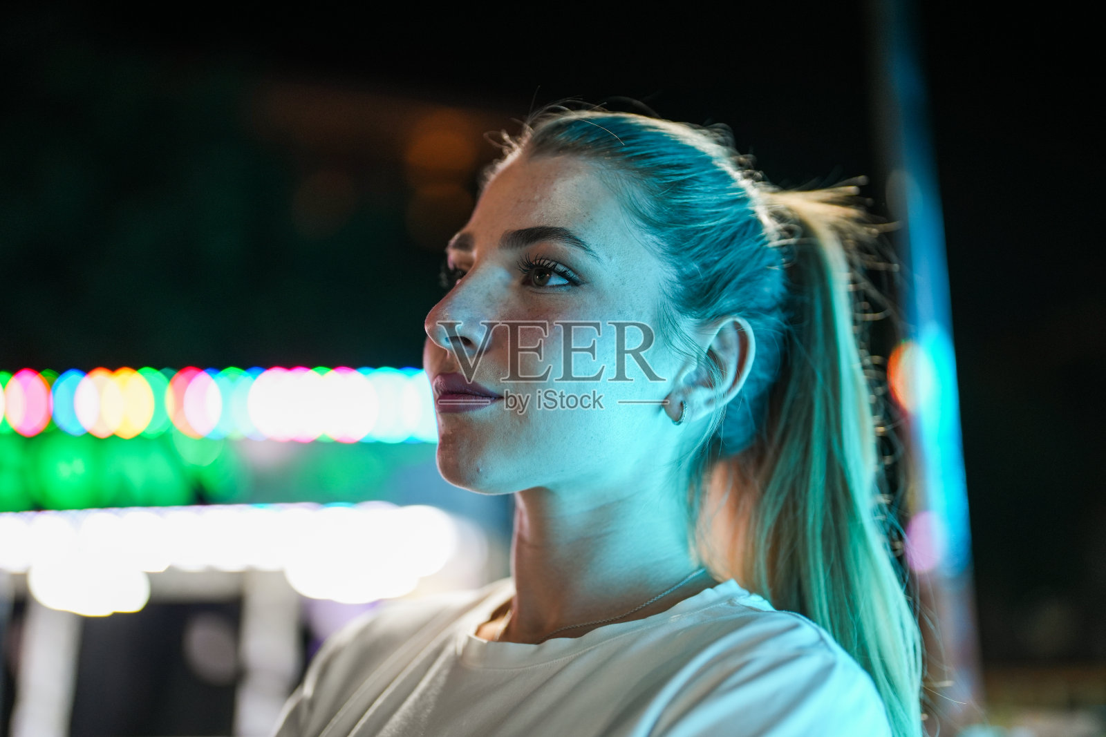 傍晚时分,年轻女子站在城市迷离的彩灯前的肖像照片摄影图片