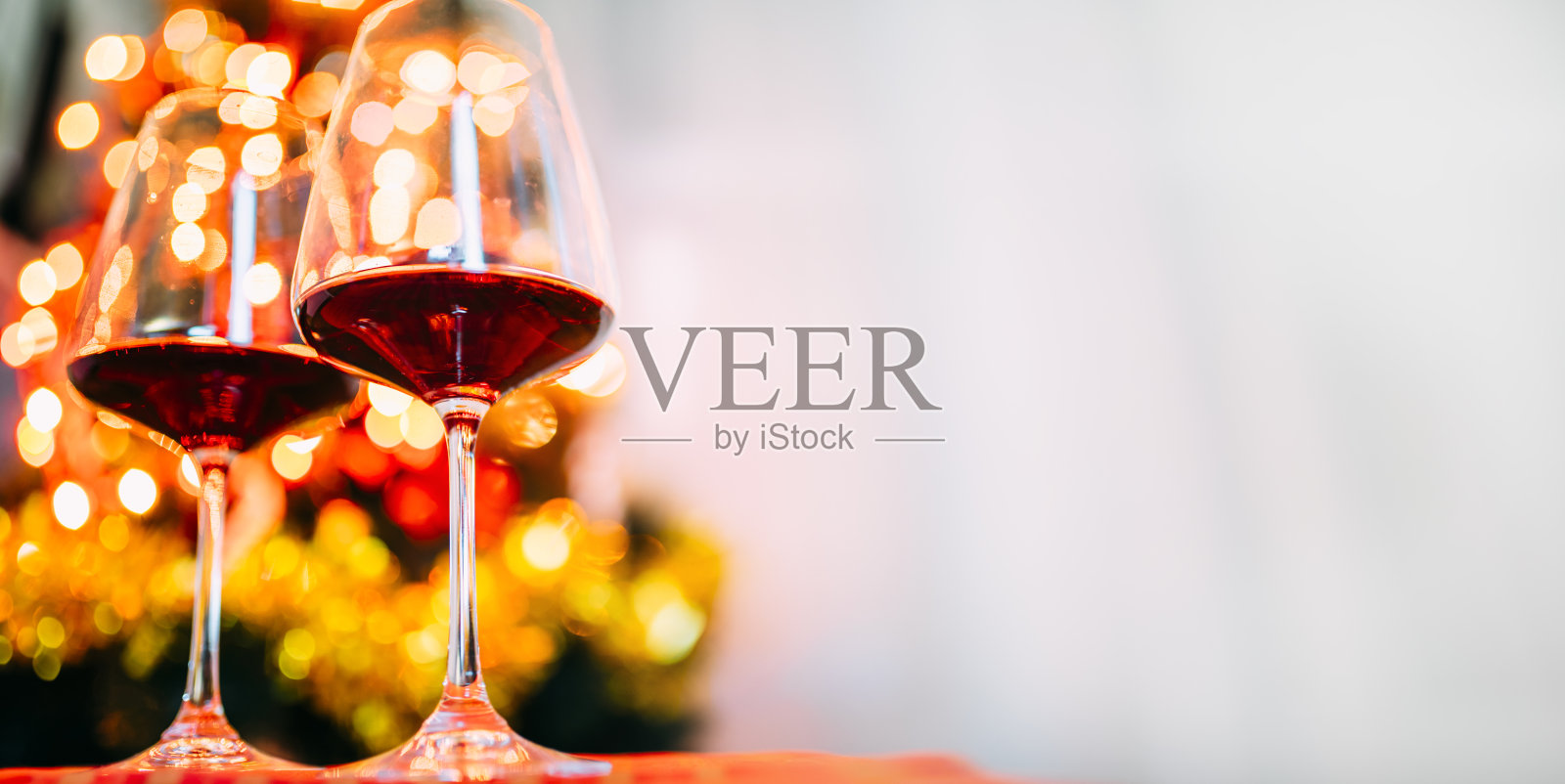 两杯红酒在圣诞树的彩灯前散景。新年前夕和圣诞节庆祝晚会。照片摄影图片