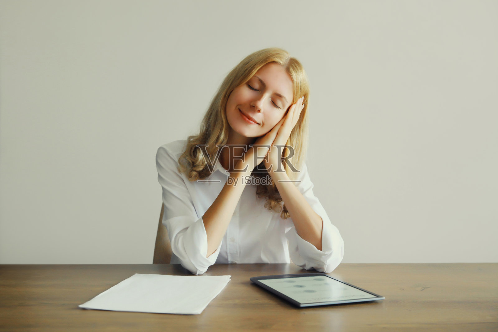 劳累过度的白人年轻女子坐在家里或办公室的办公桌前,一边用数码平板电脑和纸质文件工作,一边休息睡觉照片摄影图片