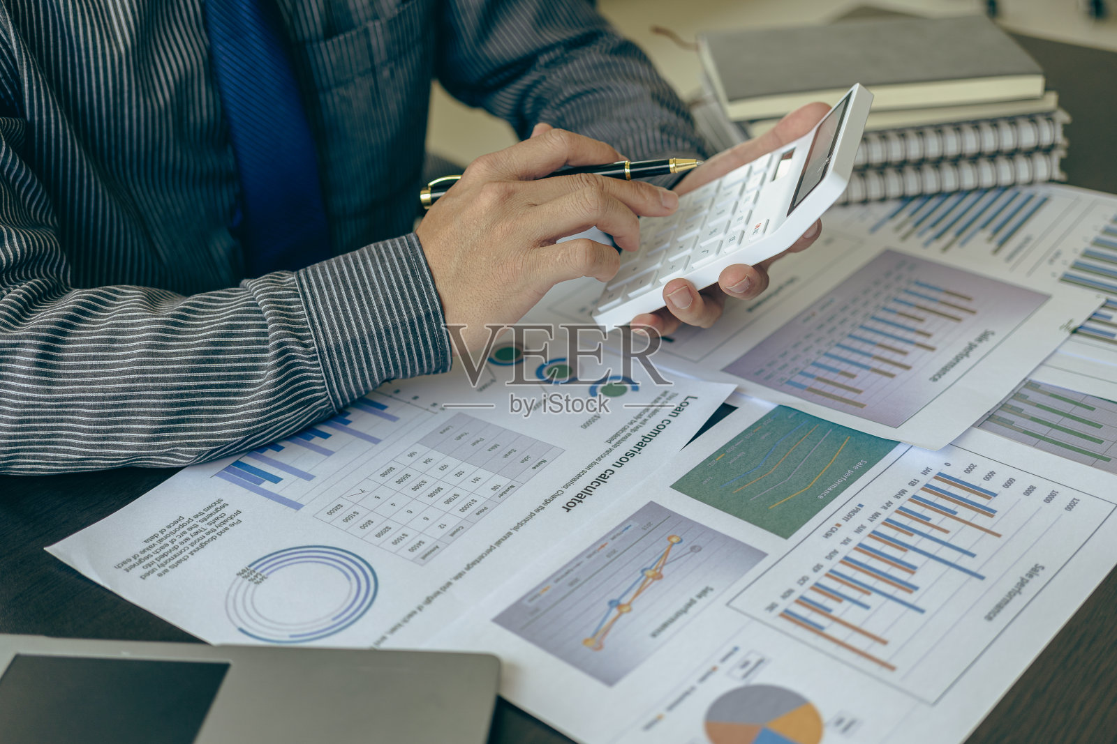 商务人员在办公桌旁用计算器计算数字,用图表、业务报告和笔记本电脑办公。特写图像照片摄影图片