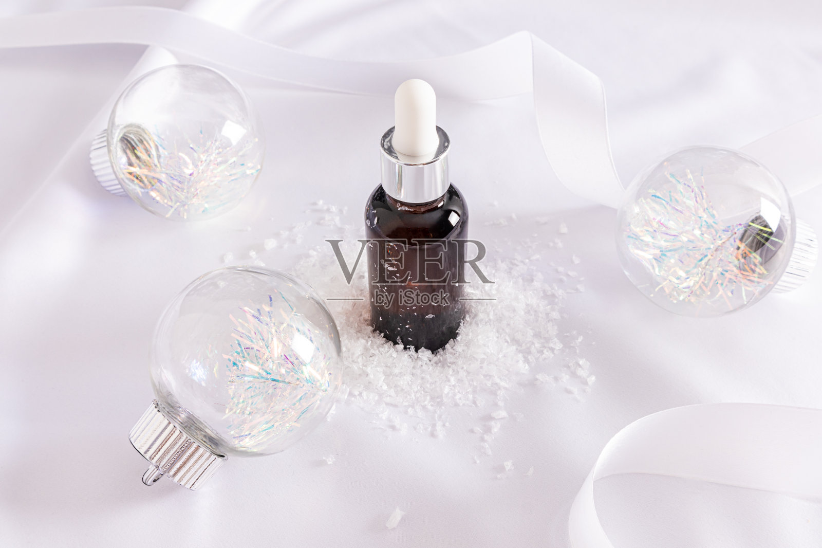 保湿精华液装在一个带有滴管的瓶子里,用于护理抗衰老皮肤,涂在白色缎子和玻璃球上。除夕夜产品广告。照片摄影图片