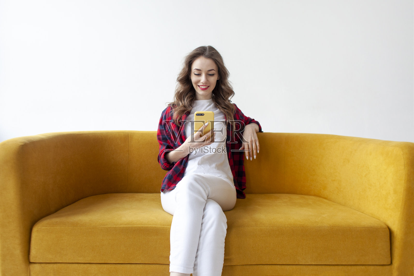 年轻可爱的女孩在柔软舒适的沙发上使用智能手机,女人正在网上用手机打字照片摄影图片