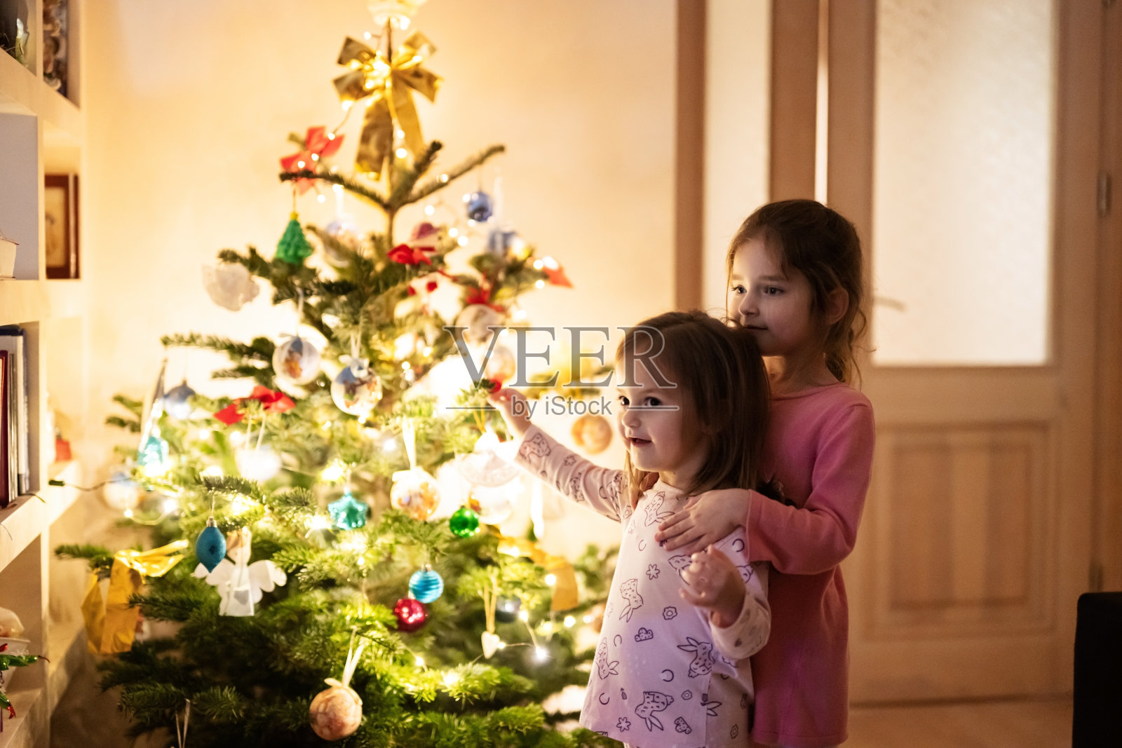 两姐妹晚上一起在圣诞树旁回家。照片摄影图片