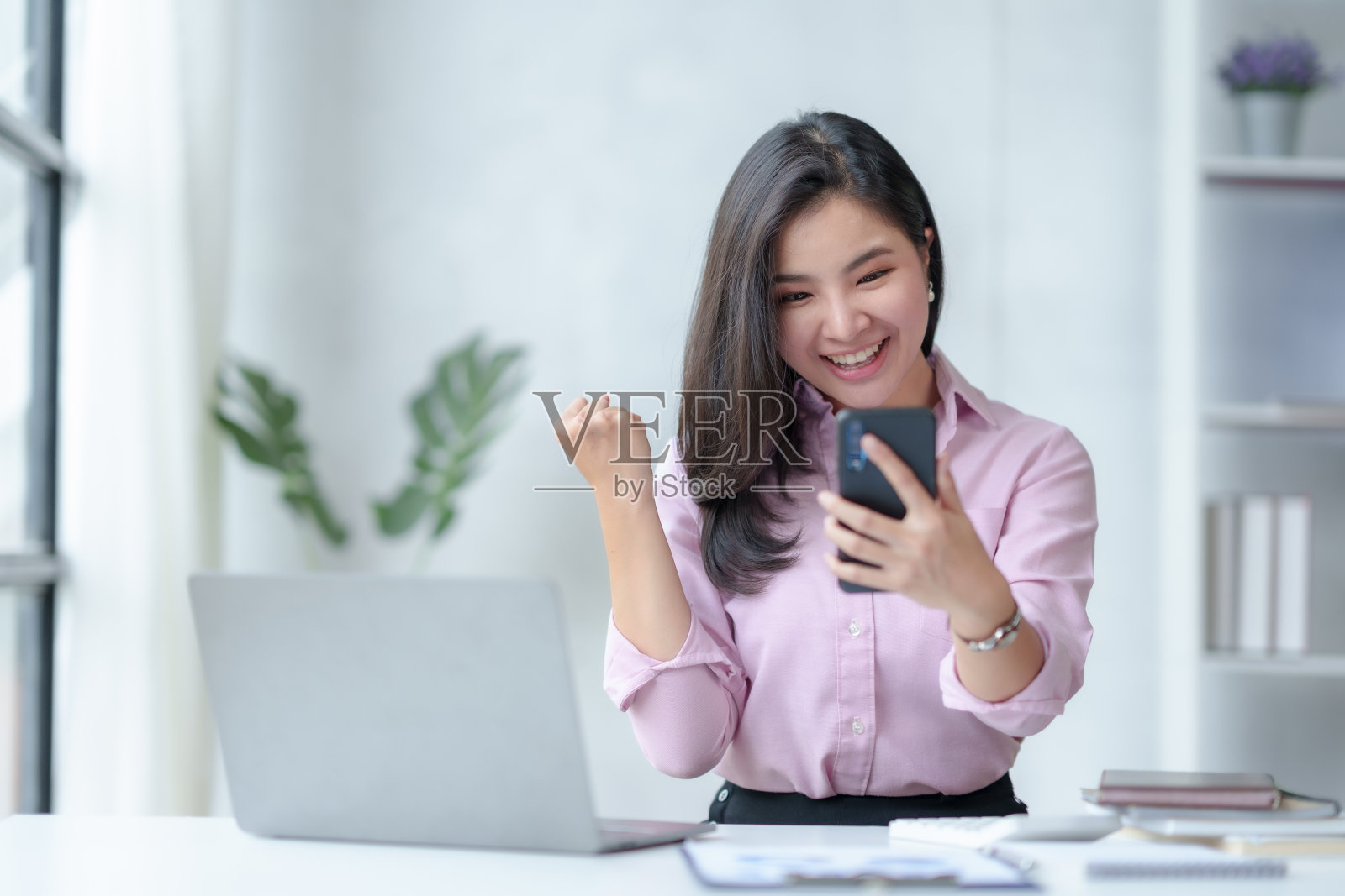 美丽的亚洲女商人使用智能手机,为她通过办公室手机取得的成功感到高兴和兴奋。照片摄影图片