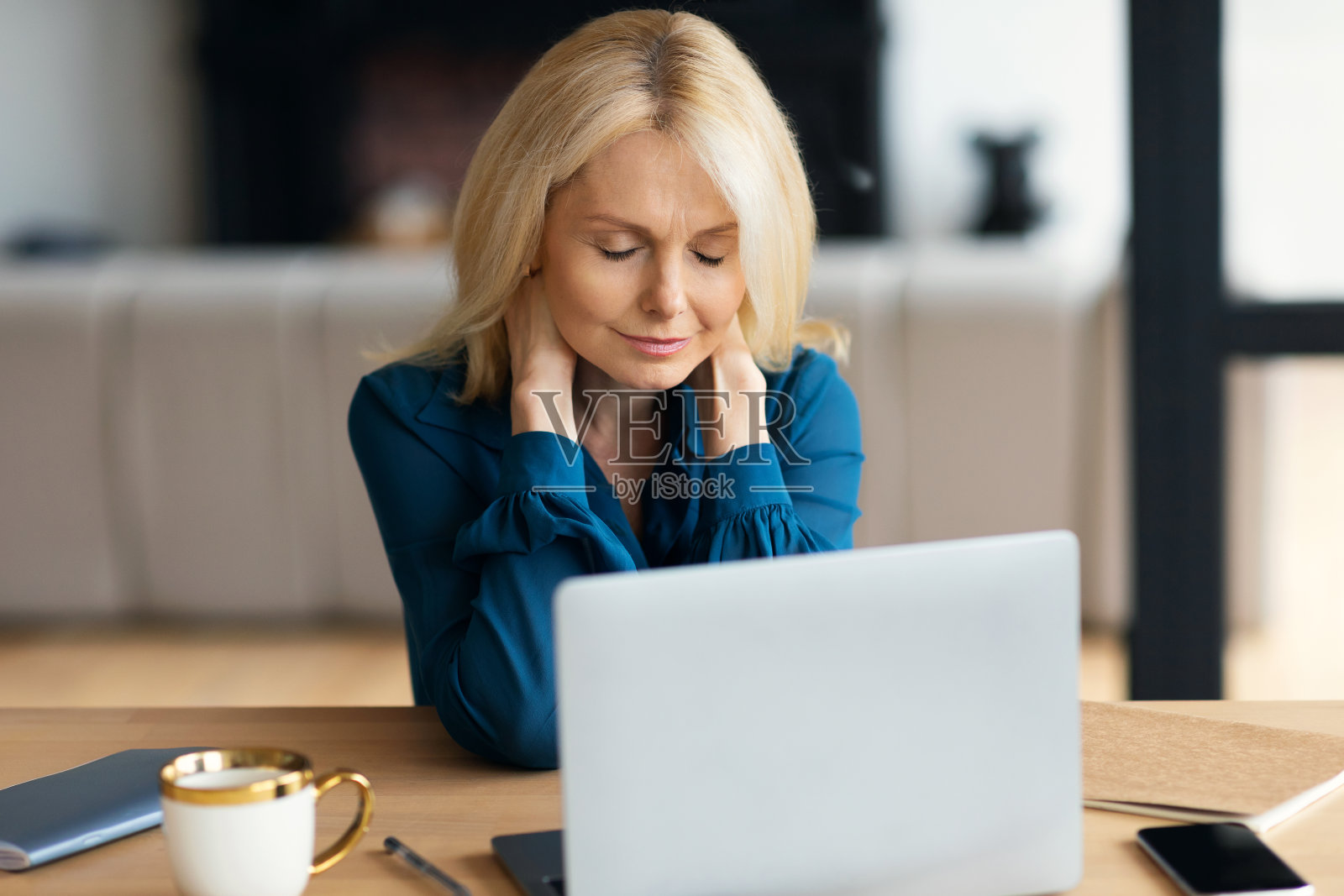 疲惫的成熟女商人在笔记本电脑上工作,揉着脖子,患有办公室综合症,在家室内照片摄影图片