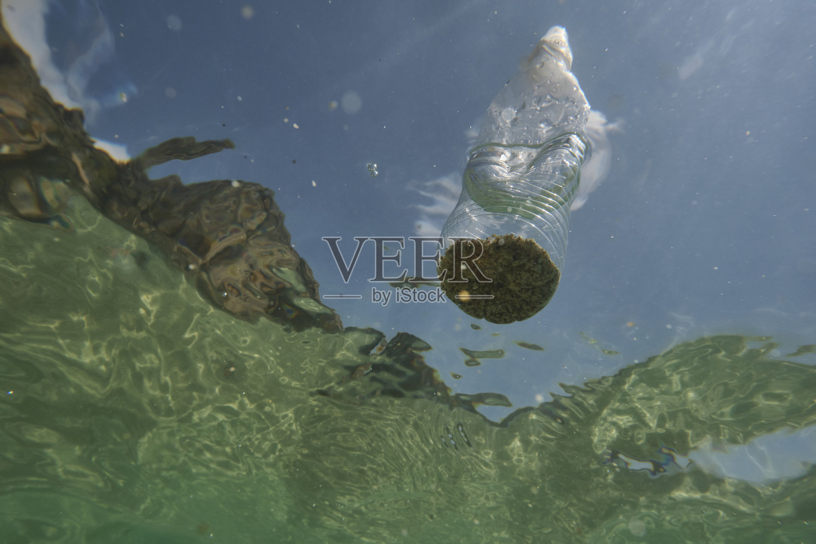 水下俯瞰海面,海面上漂浮着一个废弃的废旧塑料水瓶。照片摄影图片