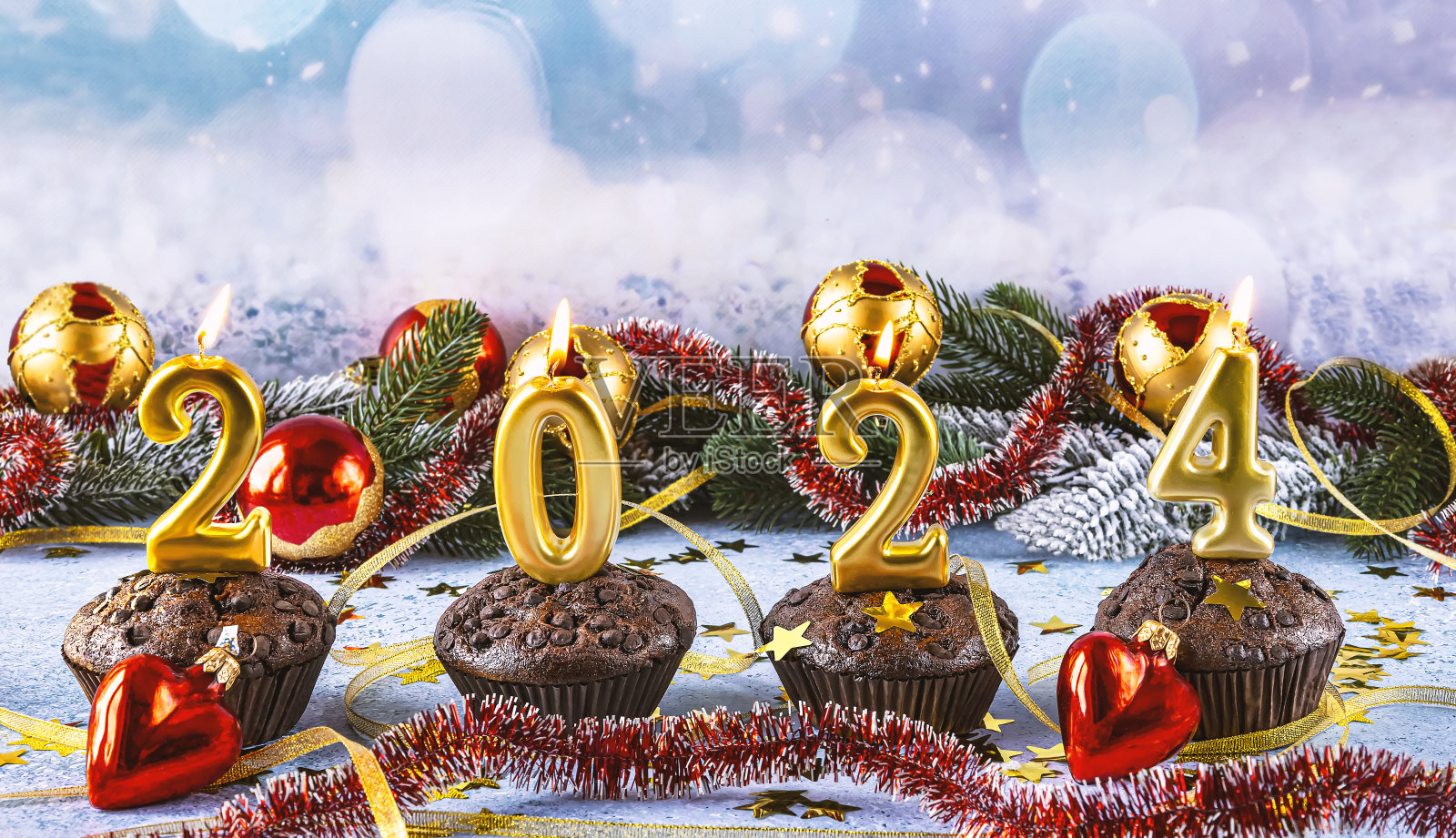2024年新年快乐概念。明亮的蜡烛、巧克力松饼、红色的圣诞球和金色的五彩纸屑照片摄影图片
