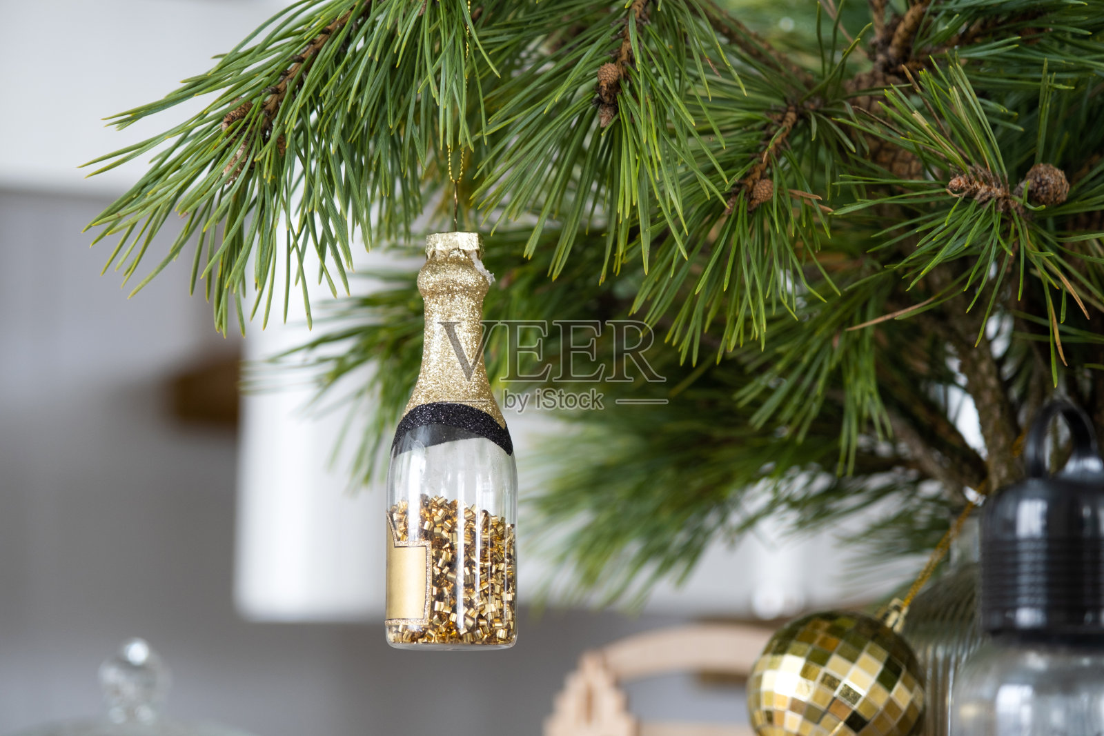 圣诞树上的一瓶起泡酒是一个玩具,挂在天然的松枝上,为圣诞节和新年做准备。玻璃装饰,环保照片摄影图片